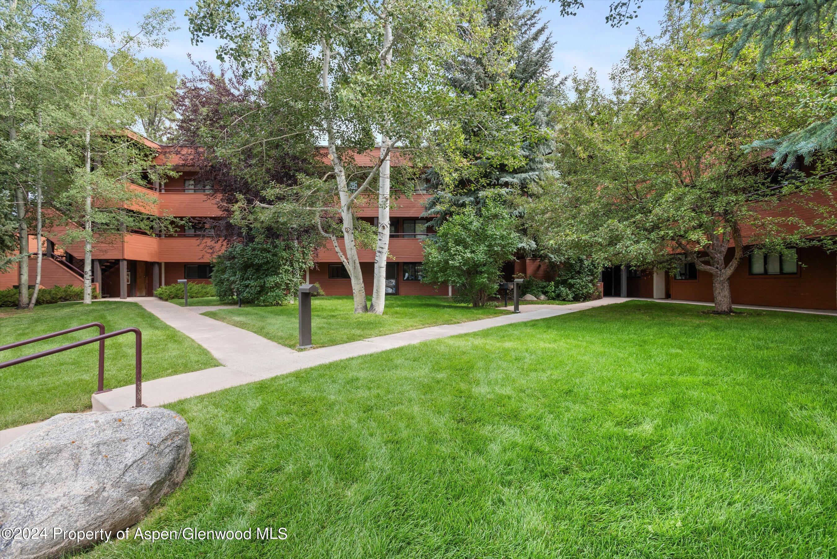 Wood-sided residential building with balconies behind a green lawn and mature trees.