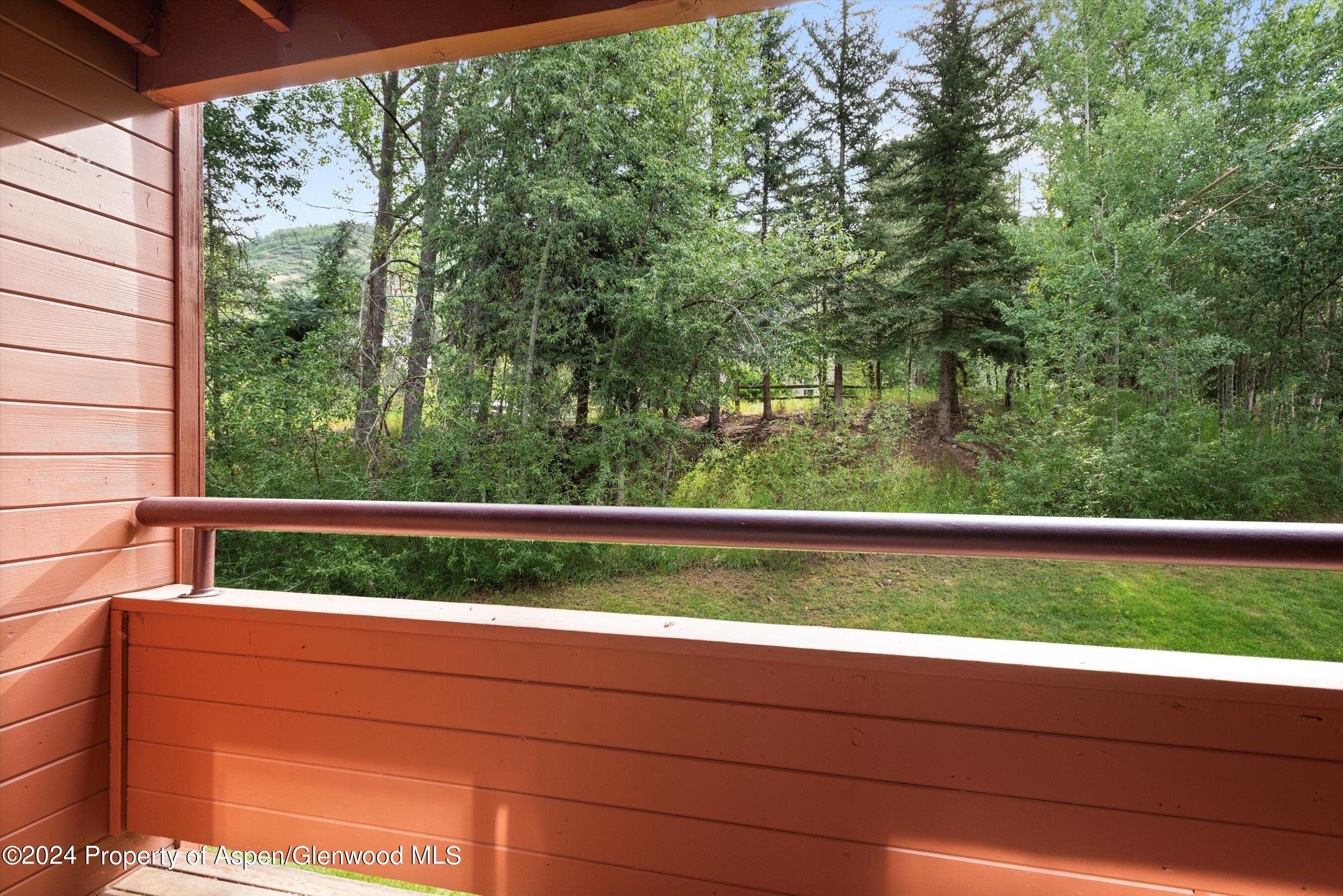 Wooden deck overlooking a grassy yard and dense trees, with a hillside visible through the foliage.