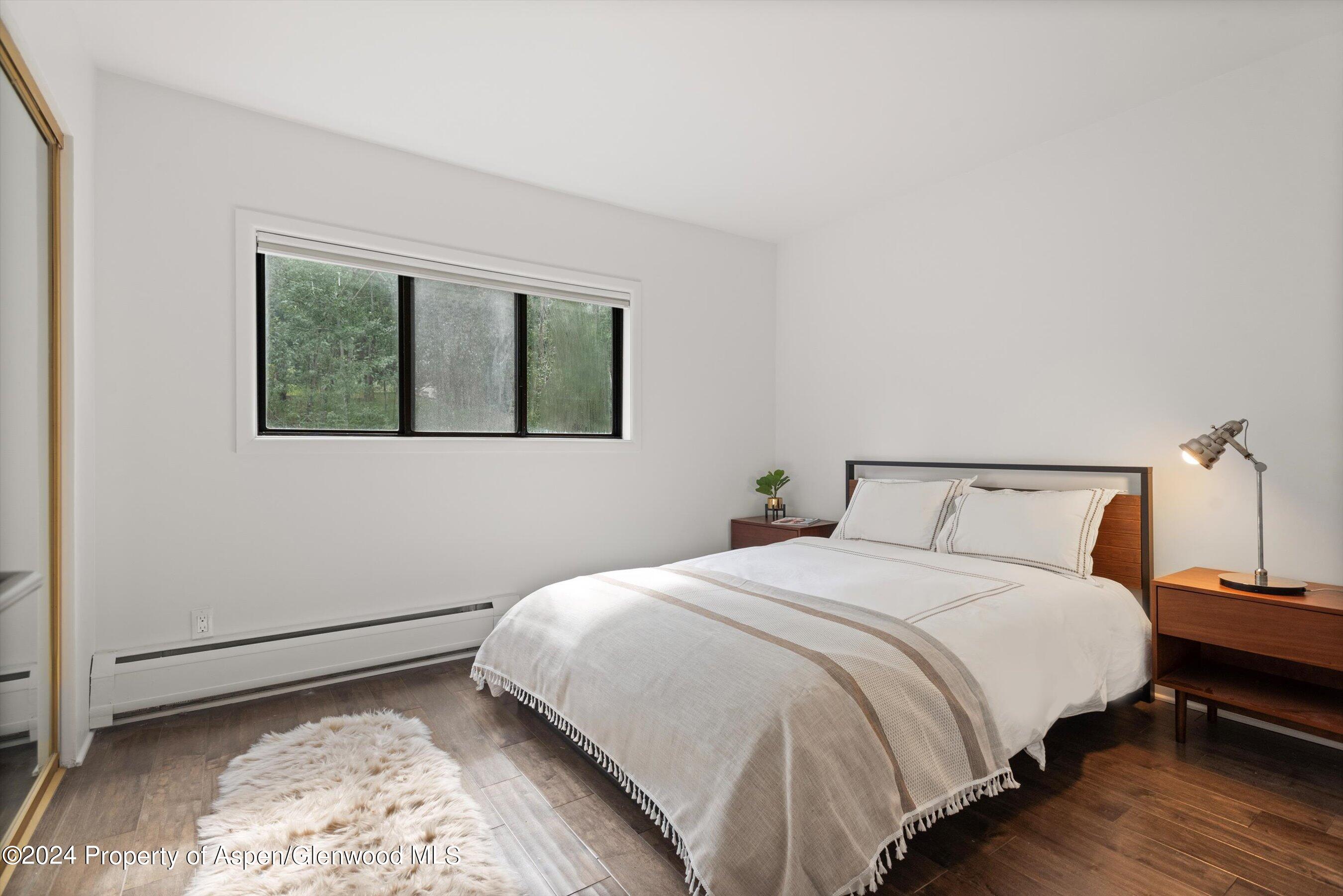 Bedroom with a white-covered bed, dark wood floor, low window, and bedside tables.
