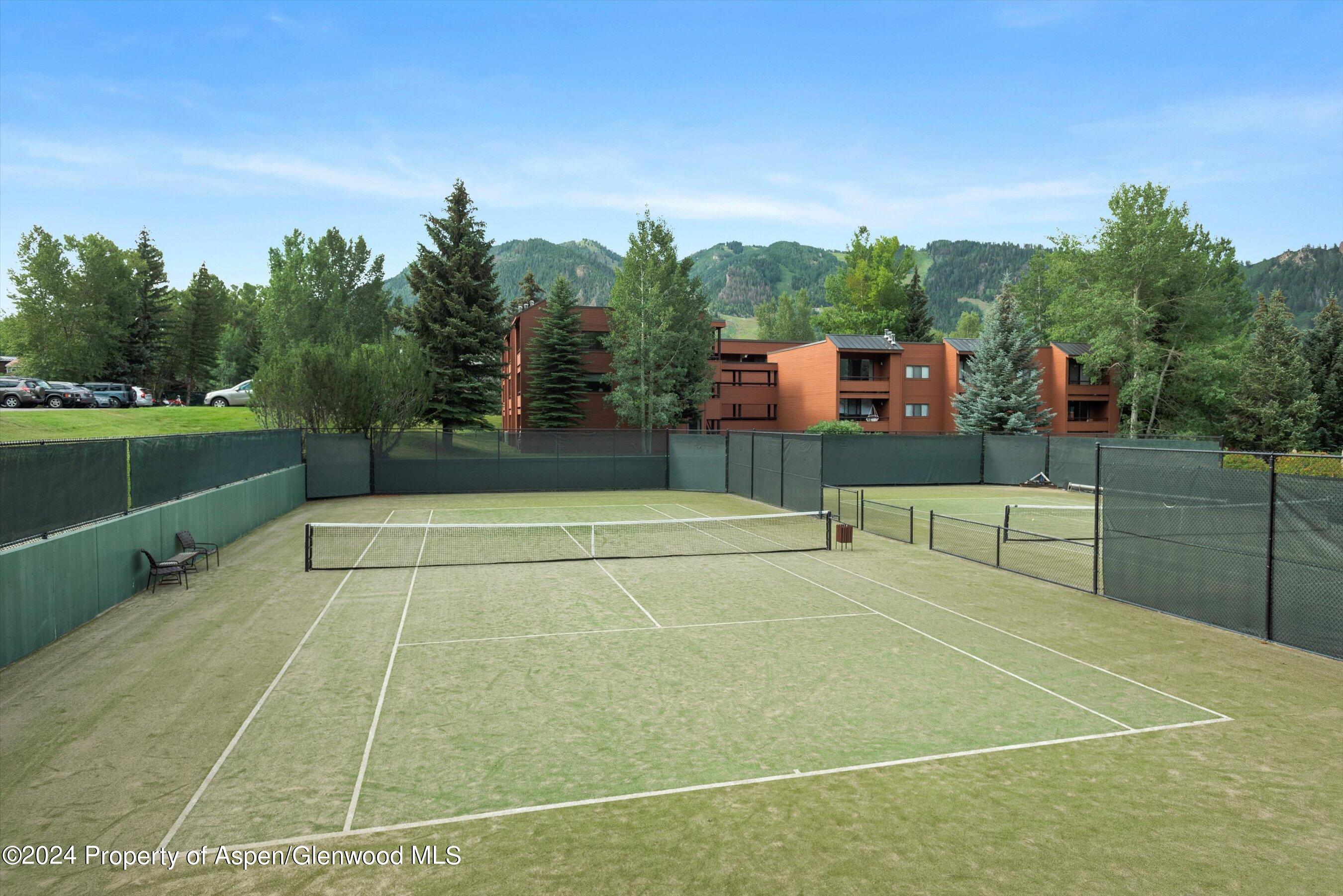 Outdoor tennis courts with a red-brown building and forested mountains behind them.