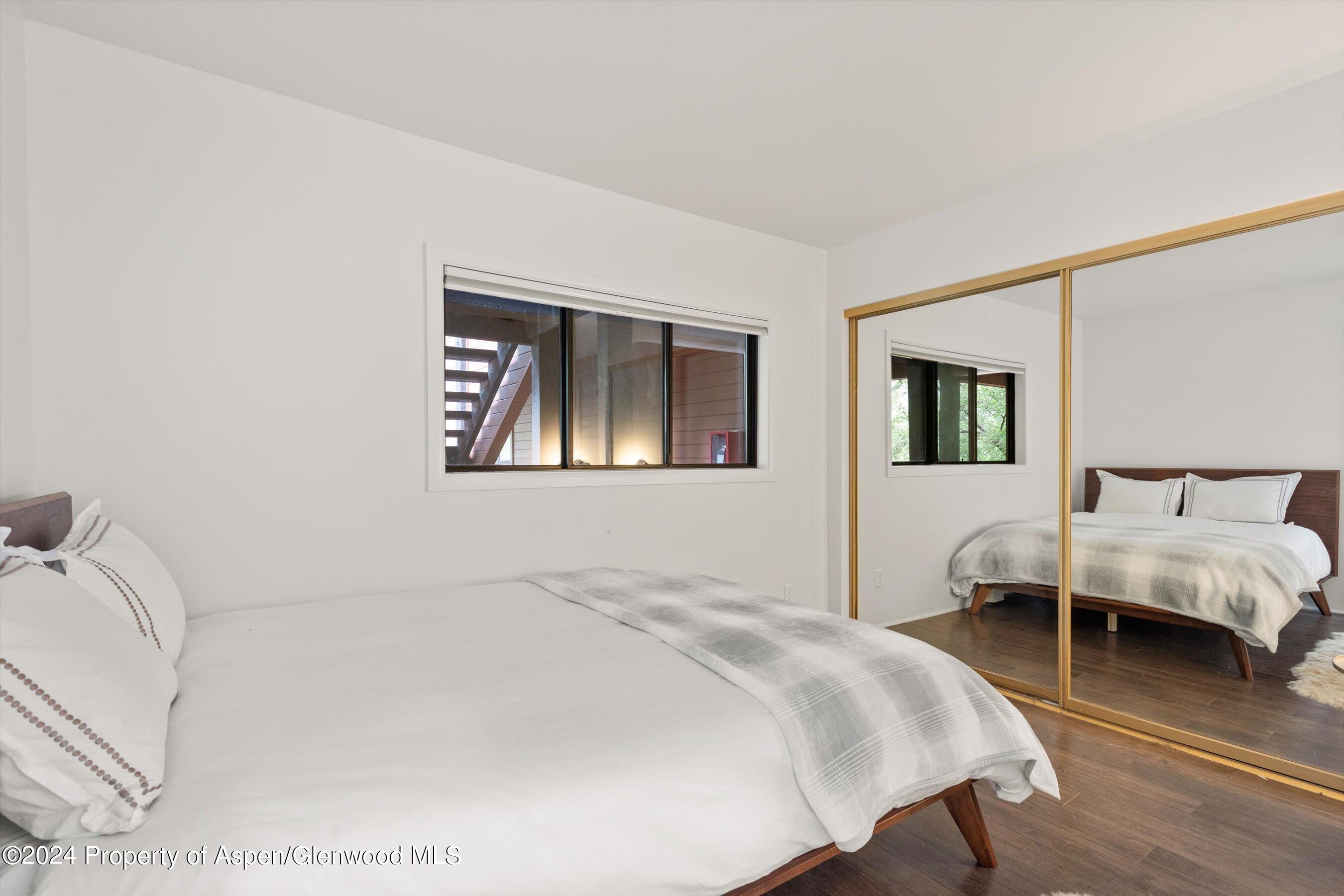 Bedroom with white bedding, dark wood floors, and mirrored closet doors.