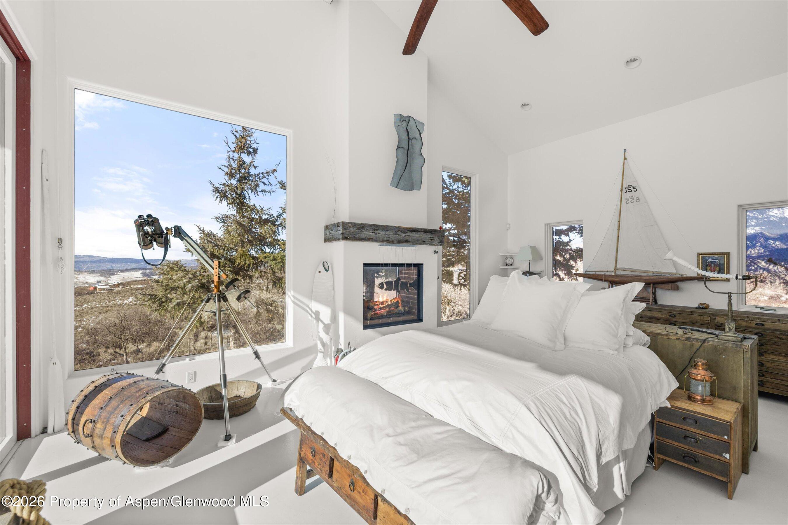Bedroom with a fireplace, telescope by a large window, and snowy mountain views.