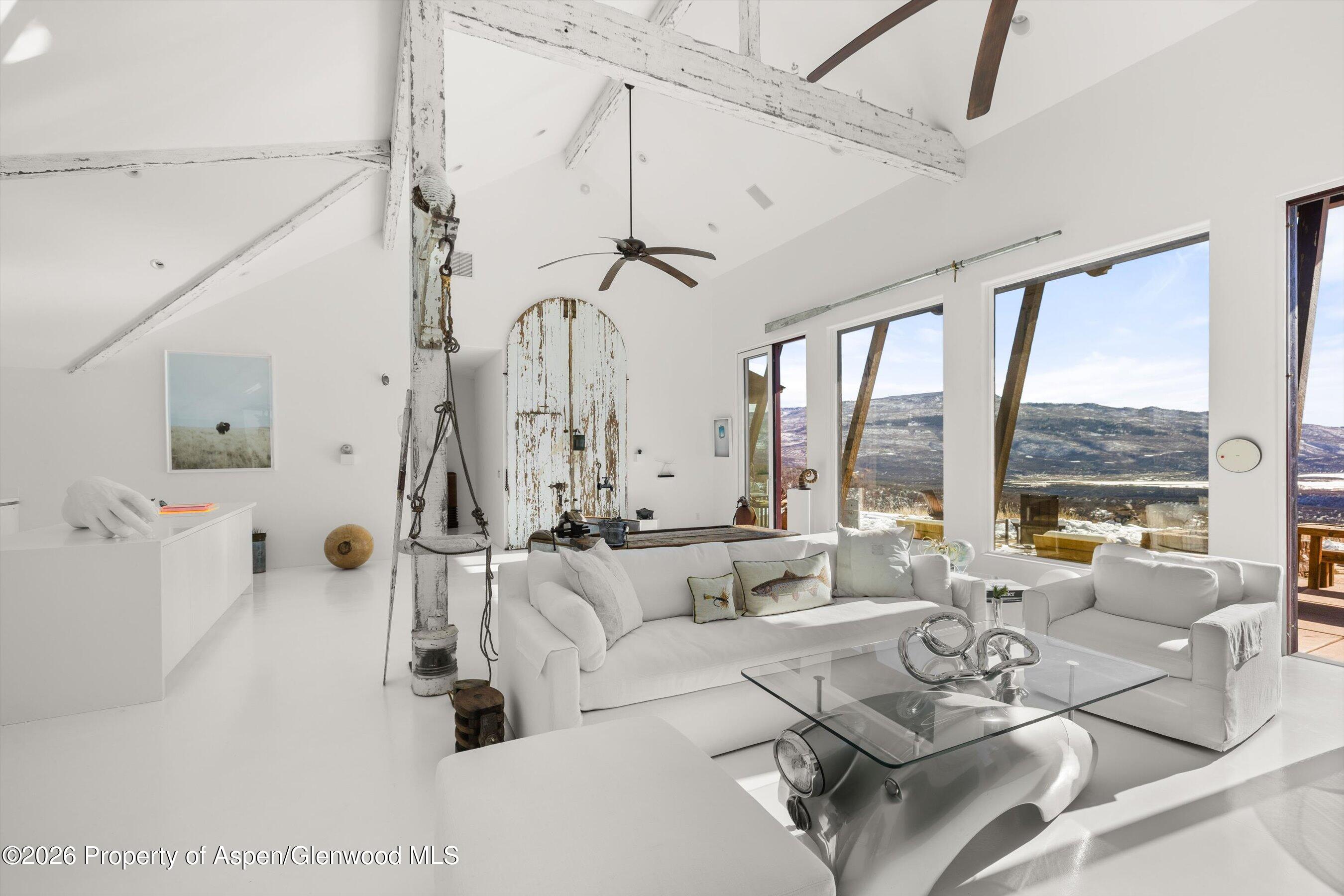 Bright living room with white sofas, vaulted timber-beam ceiling, and mountain views through large windows.