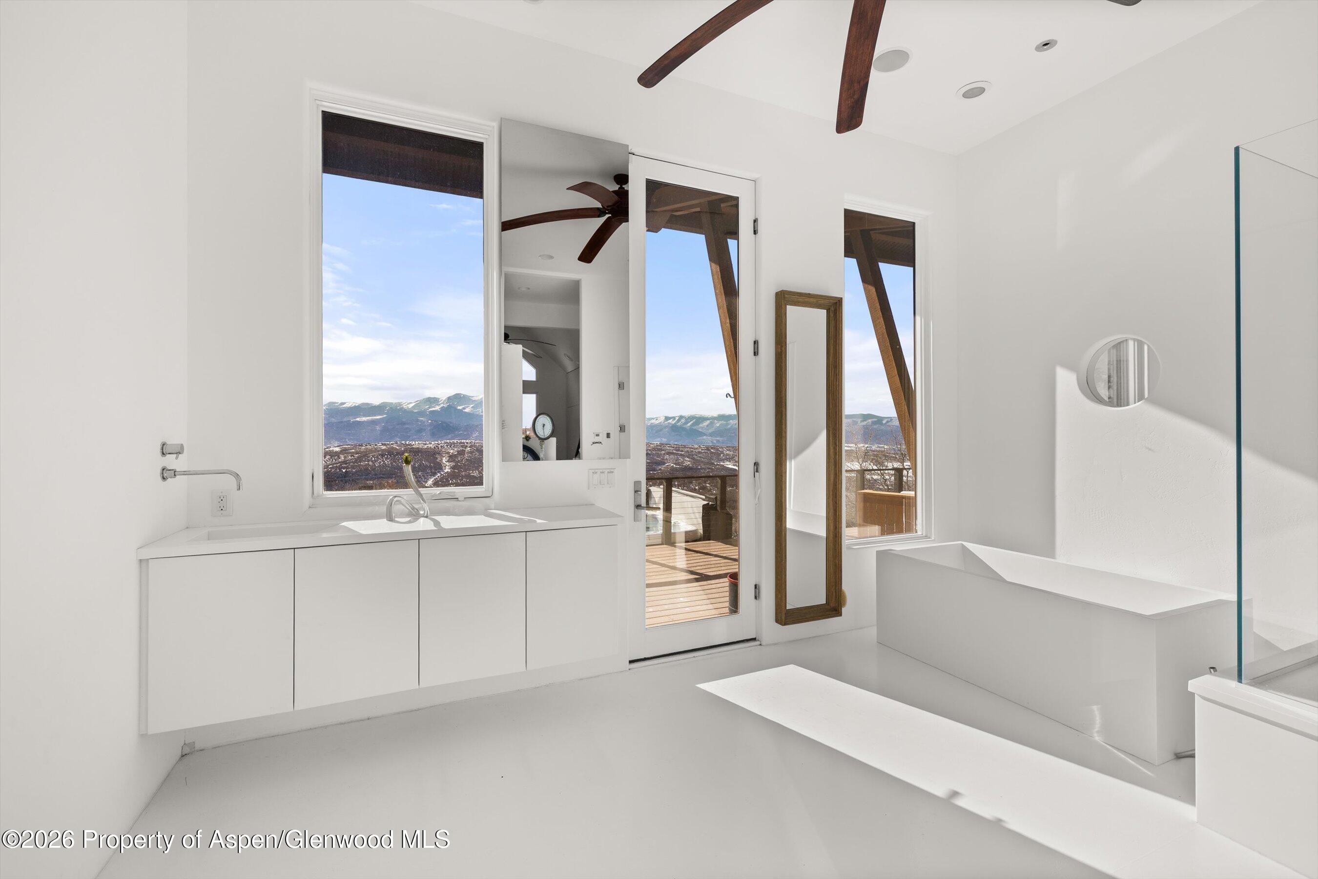 Modern white bathroom with a freestanding tub and mountain views through the windows.