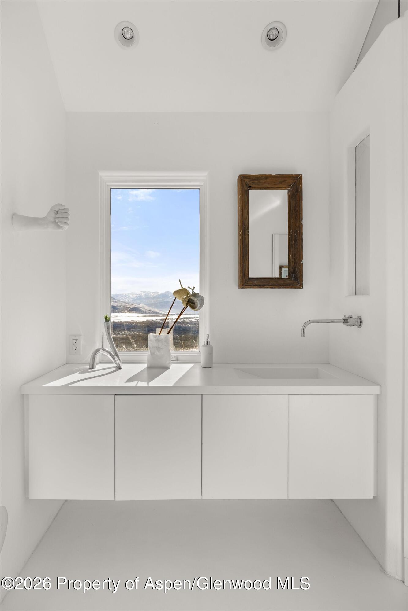 White bathroom vanity with a wood-framed mirror and mountain views through the window.