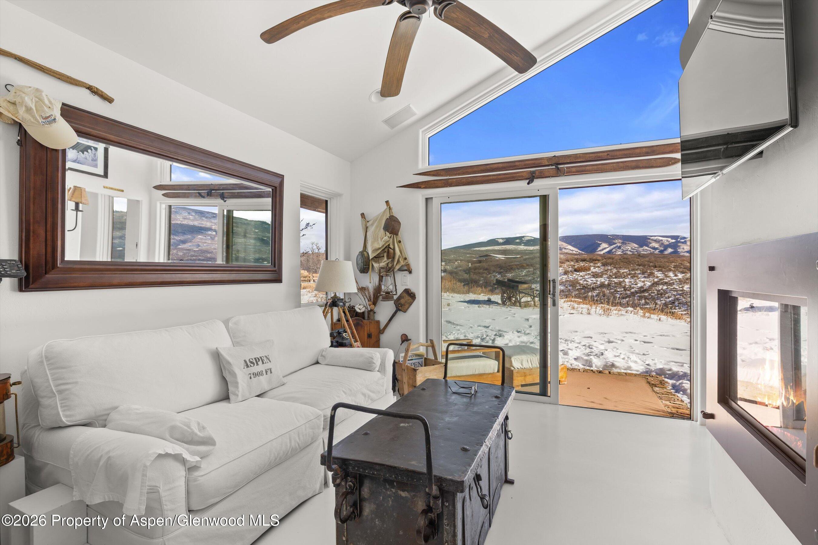 Living room with a white sofa, lit fireplace, and sliding doors overlooking snowy mountains.