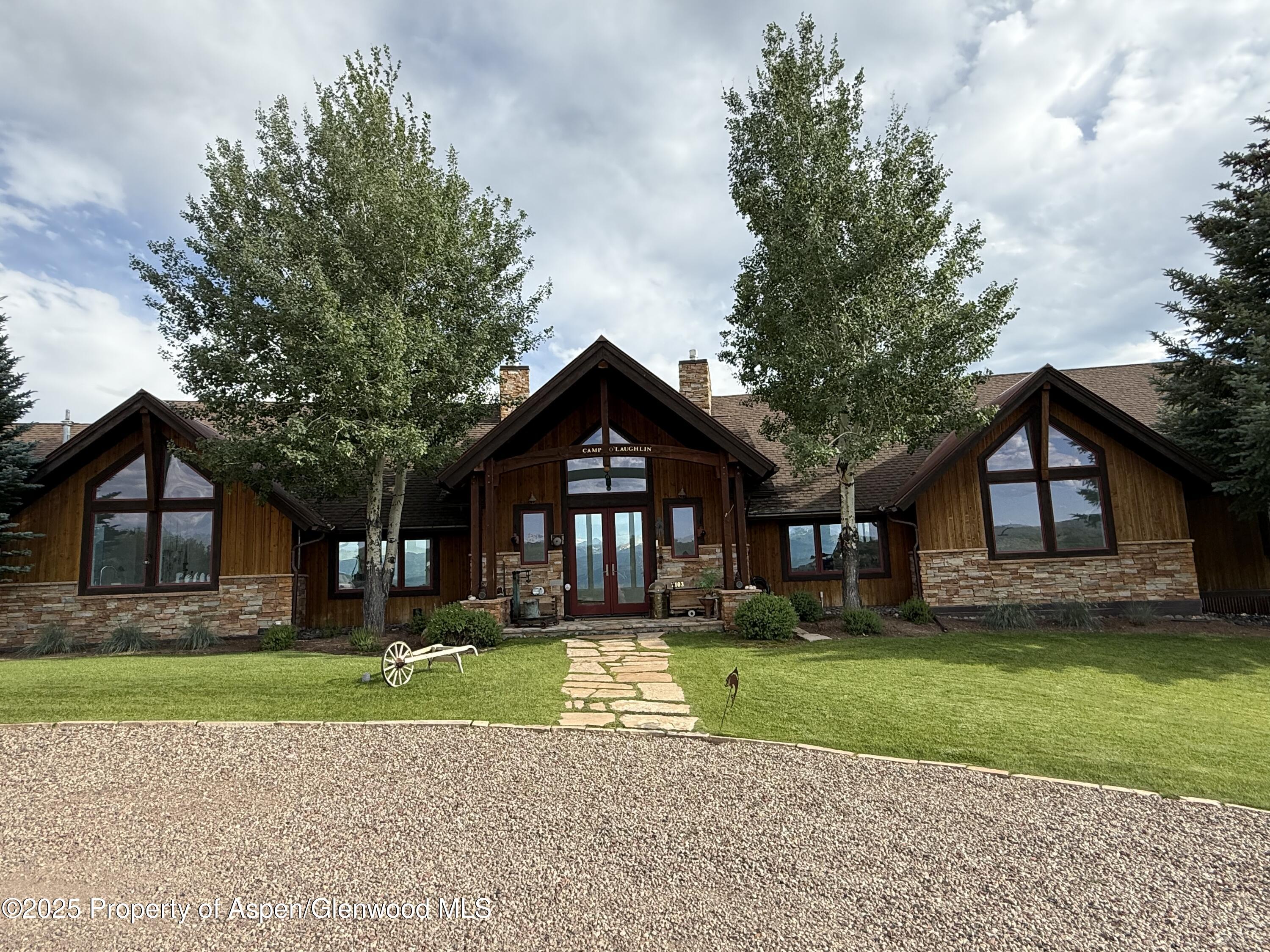 Rustic timber-and-stone home with peaked gables, mature trees, and a stone path across the lawn.