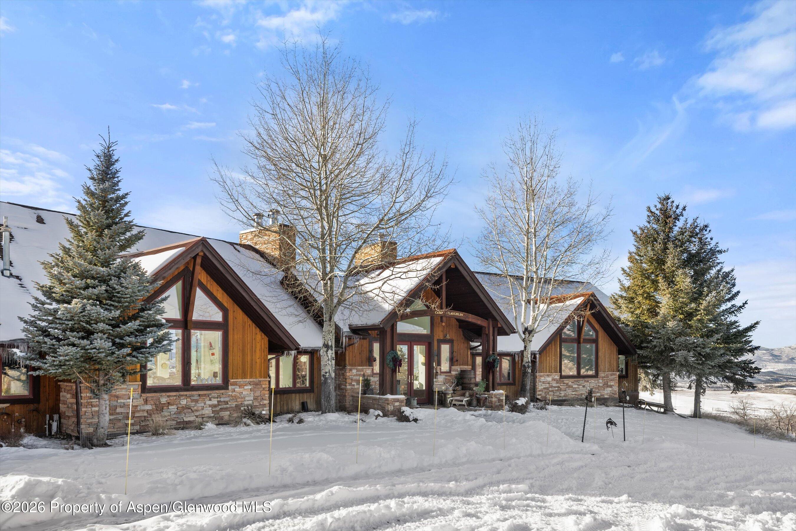 Timber-and-stone mountain home with snow-covered gabled roofs and evergreen trees.