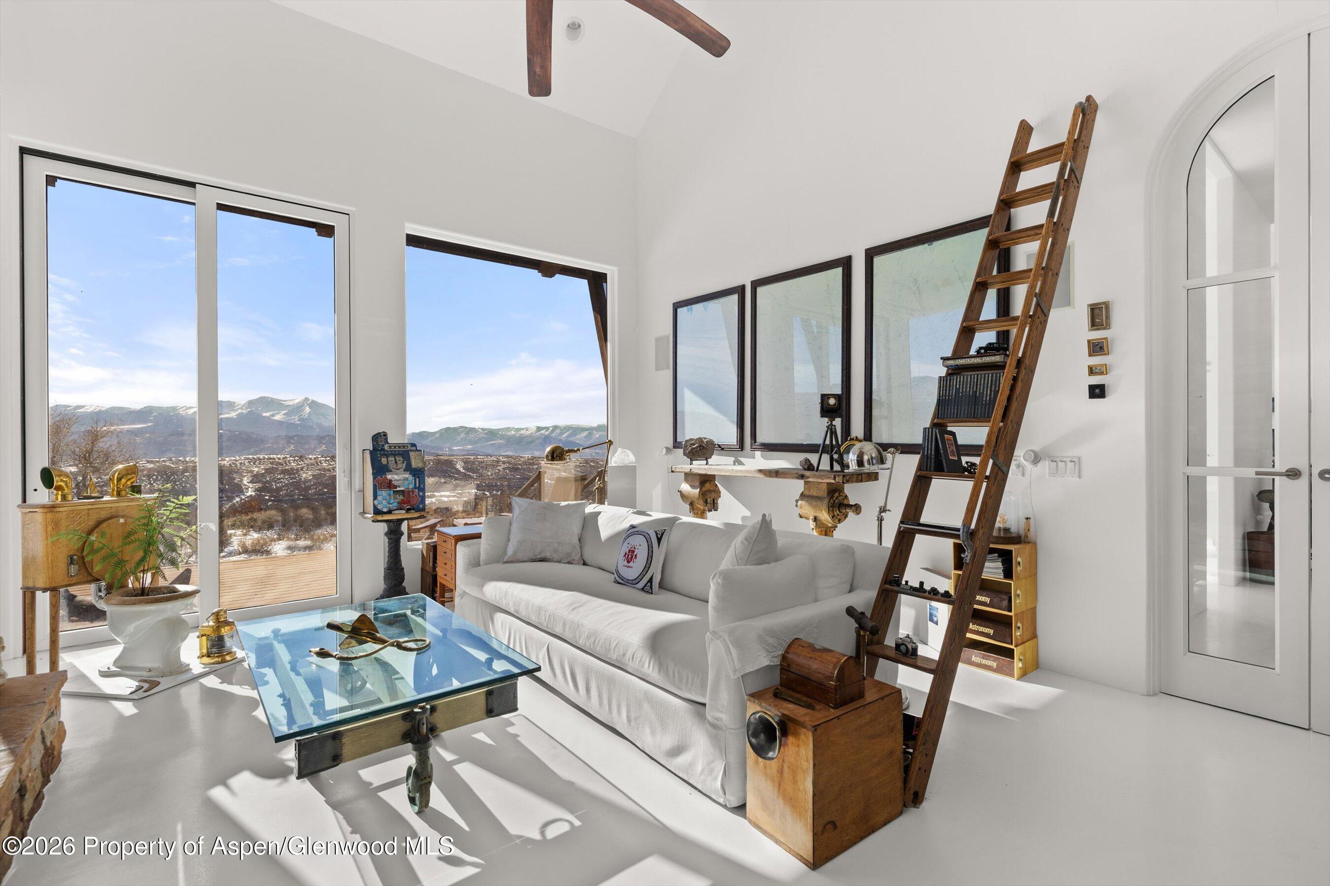 Living room with a white sofa and glass coffee table, looking out to snow-dusted mountains.