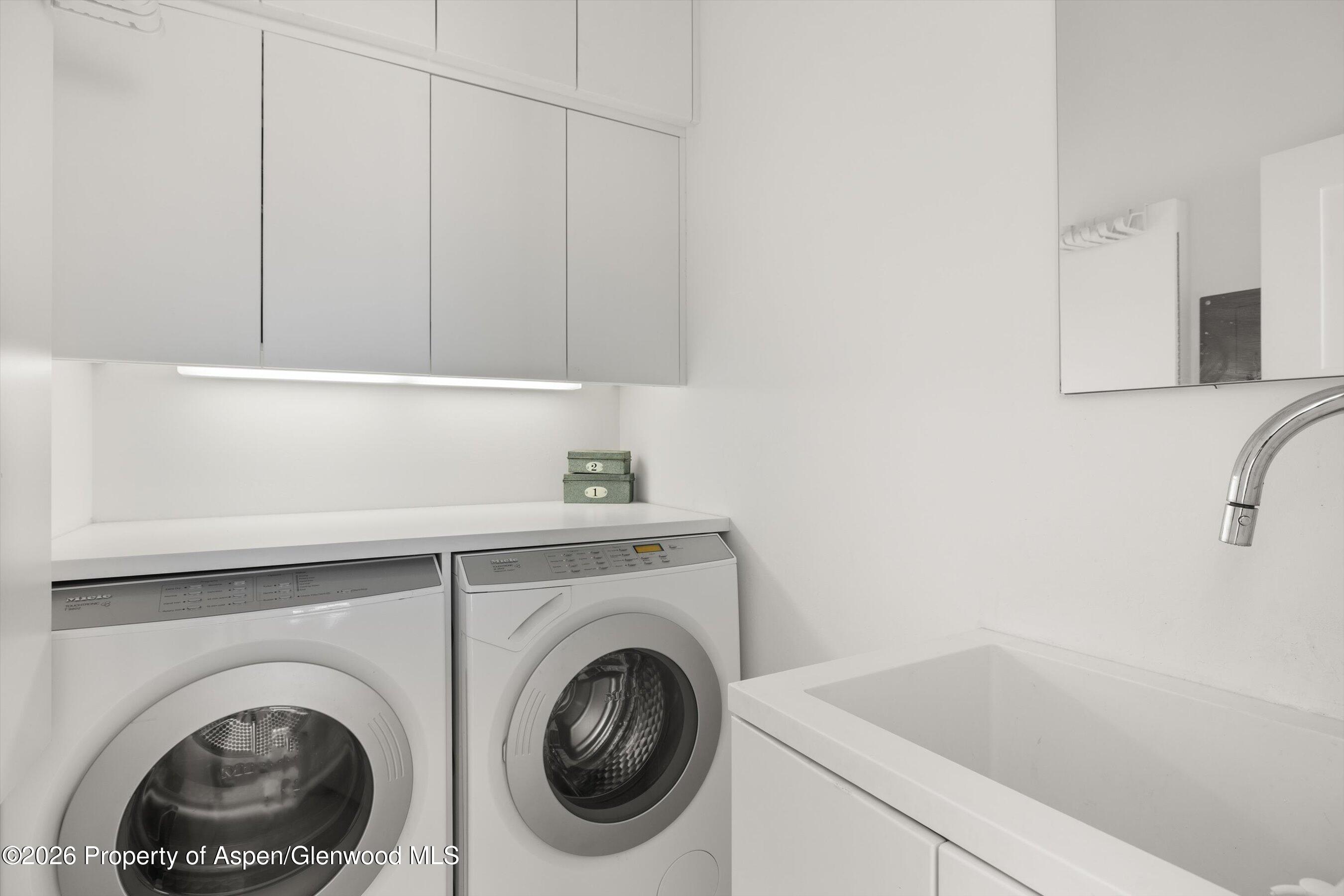 Laundry room with front-loading washer and dryer, white cabinetry, and a deep utility sink.