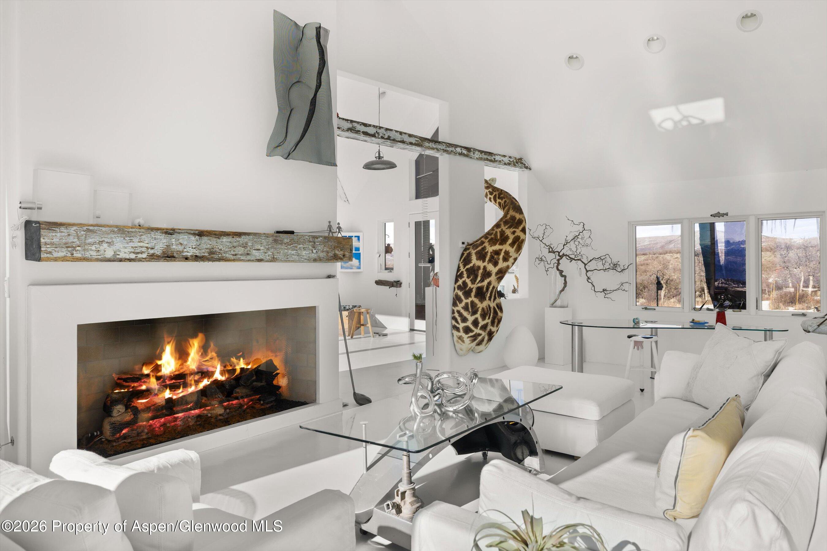 Contemporary living room with a lit fireplace, white sectional, glass coffee table, and giraffe-patterned sculpture.