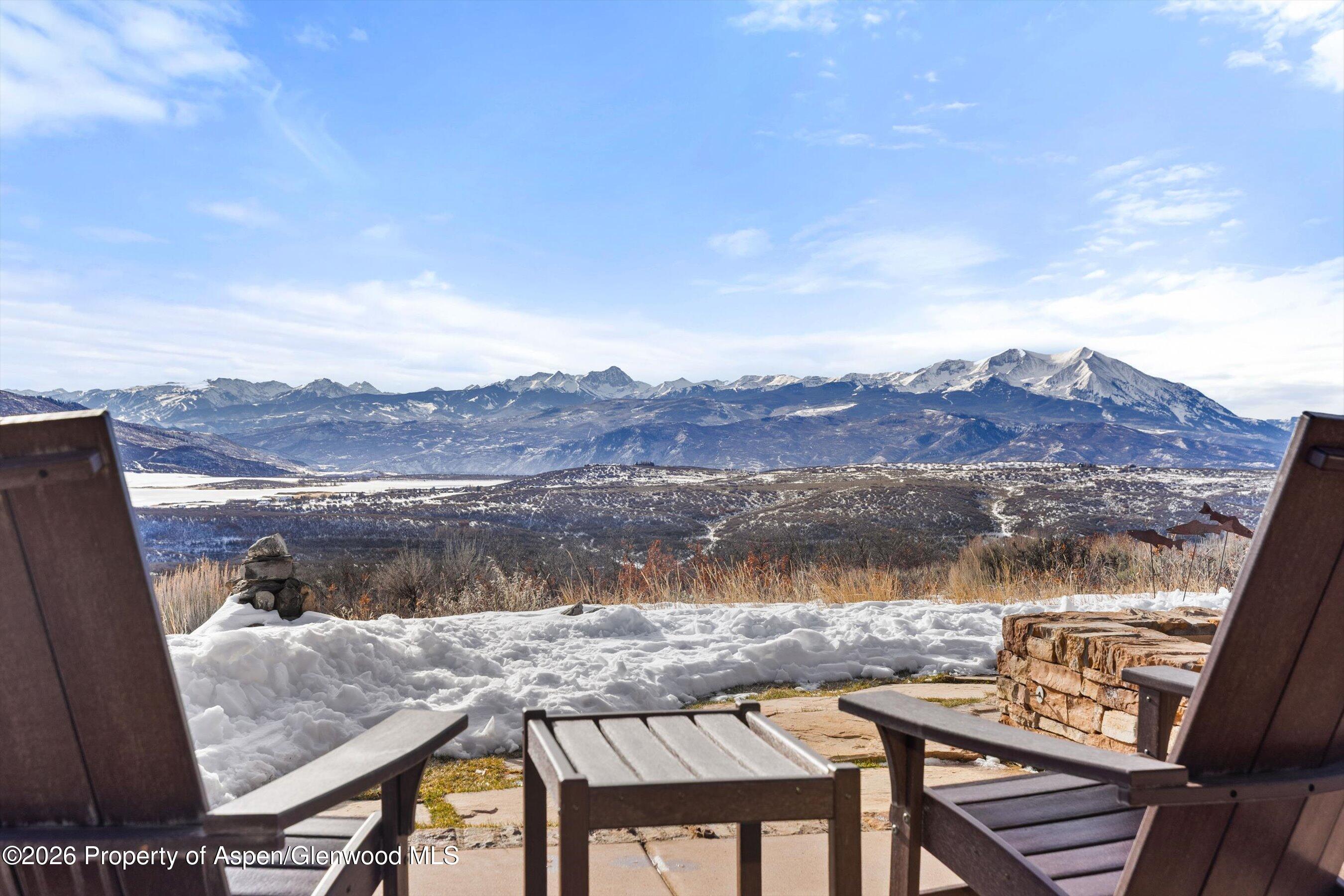 Snowy patio with Adirondack chairs overlooking a wide valley and snow-dusted mountains.
