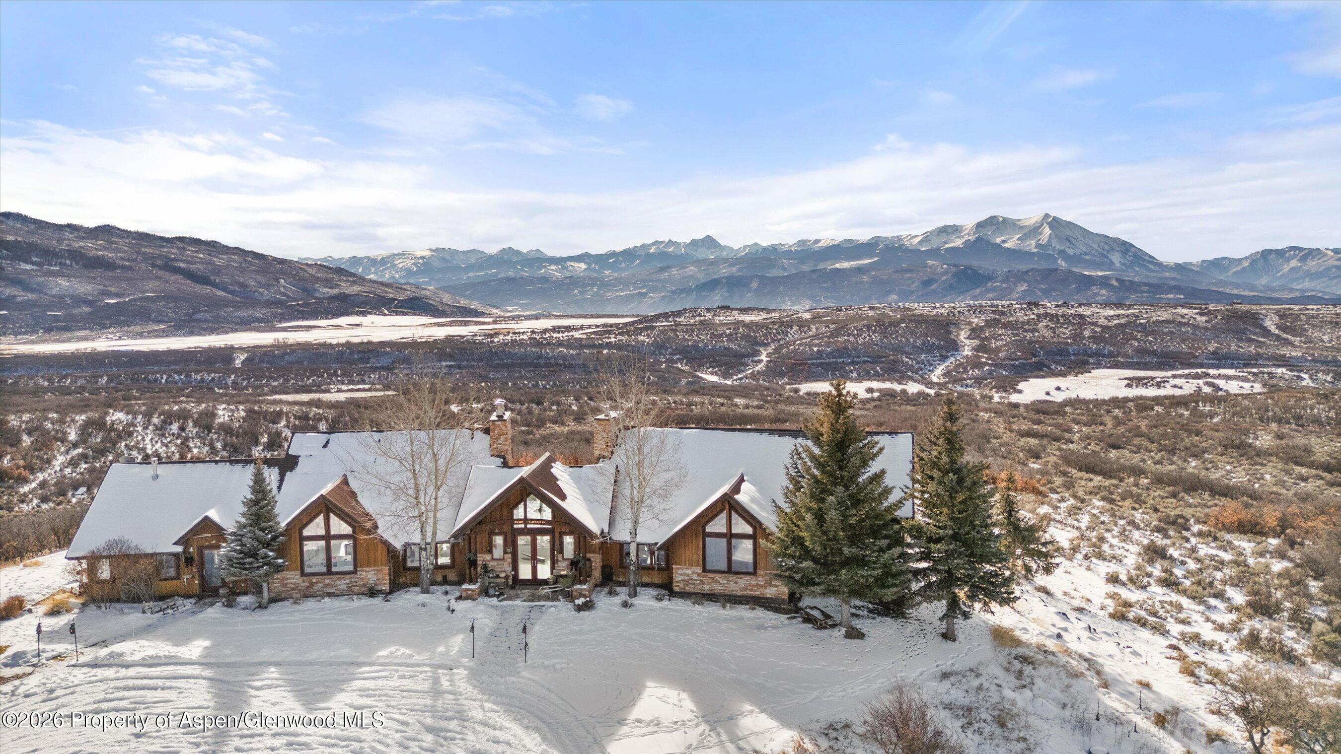 Aerial view of a snow-covered timber and stone home with mountain views.