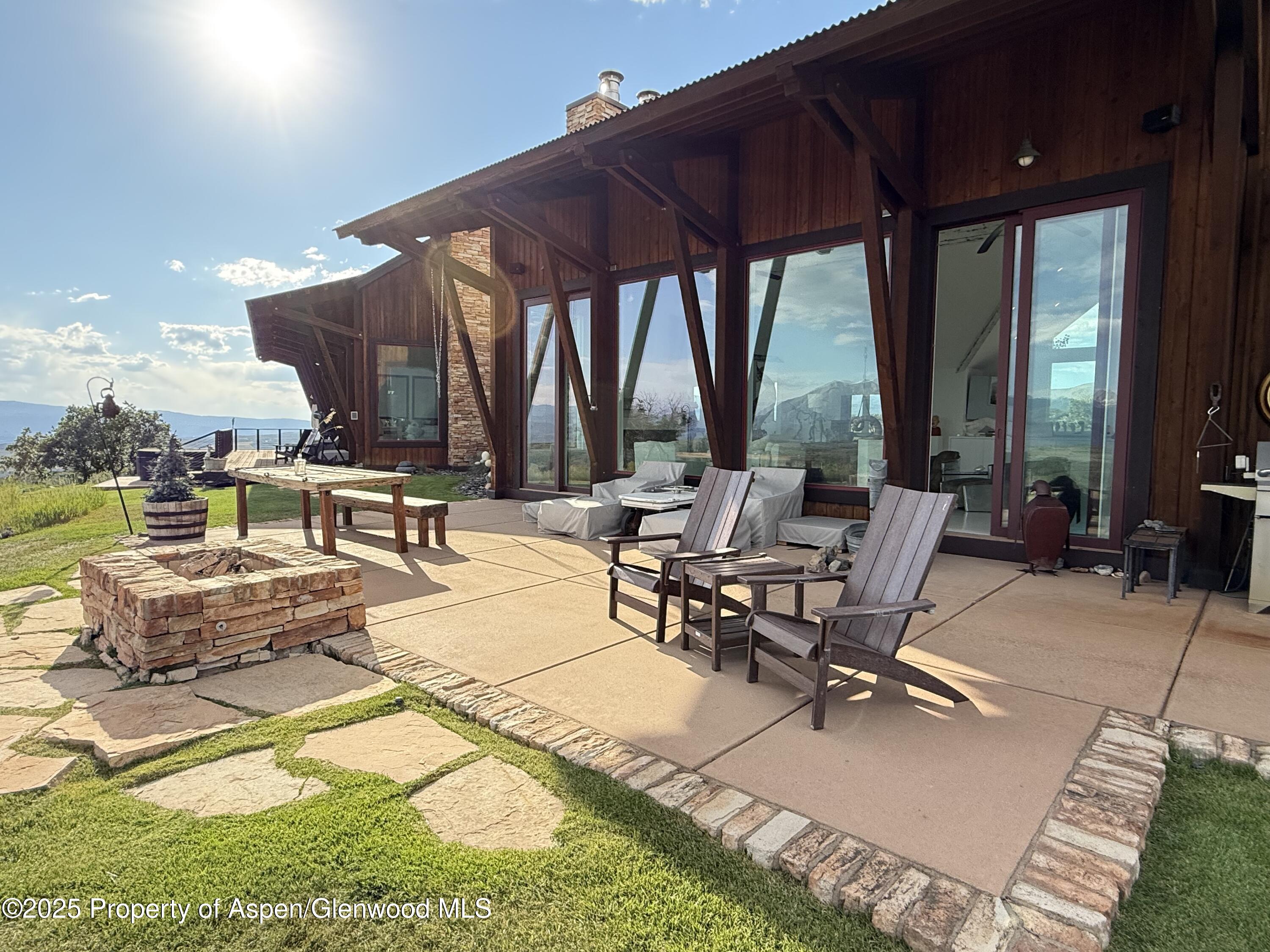 Mountain home patio with timber framing, lounge chairs, stone fire pit, and distant mountain views.