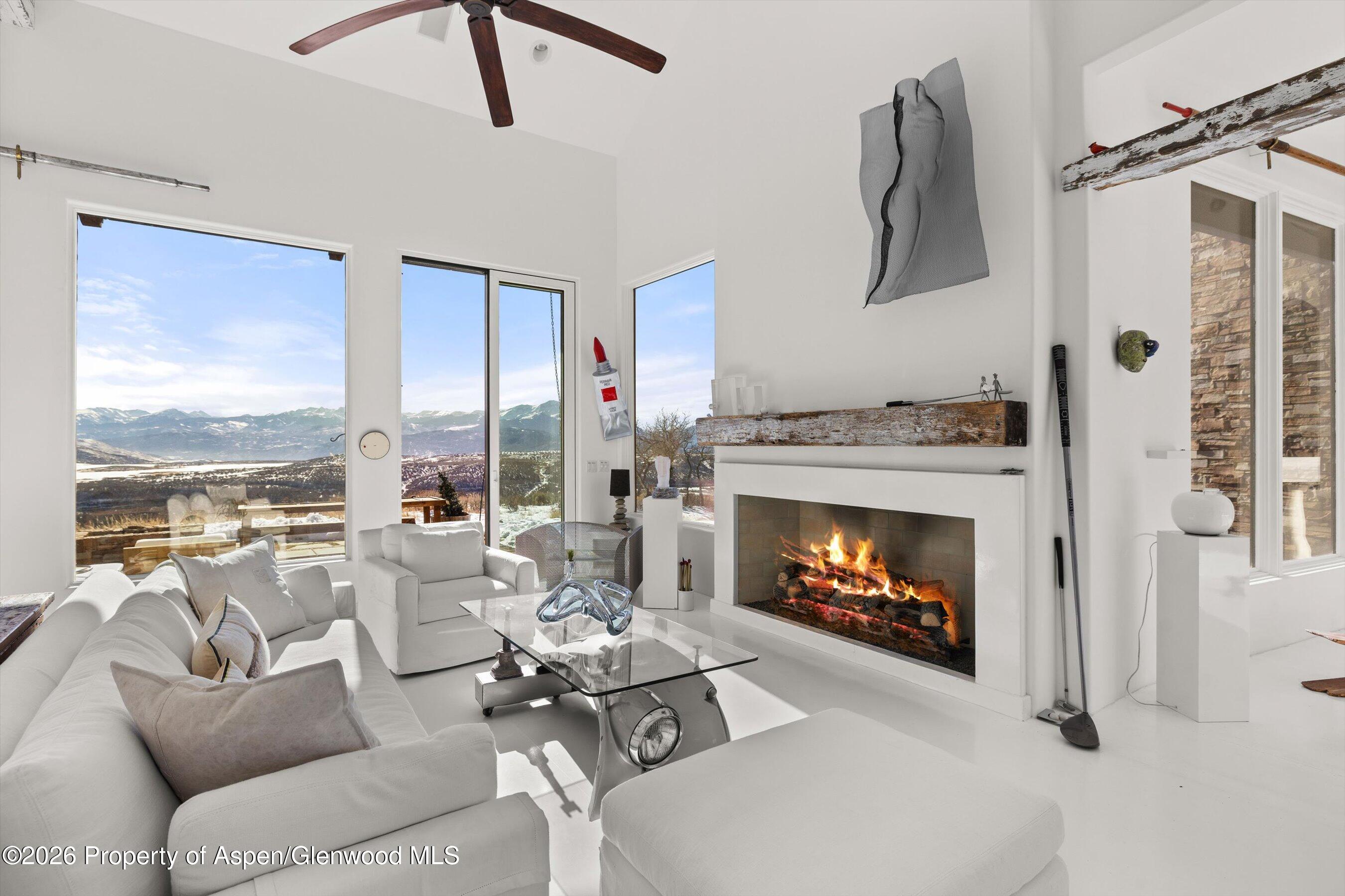 Modern living room with a lit fireplace and panoramic windows overlooking snow-dusted mountains.