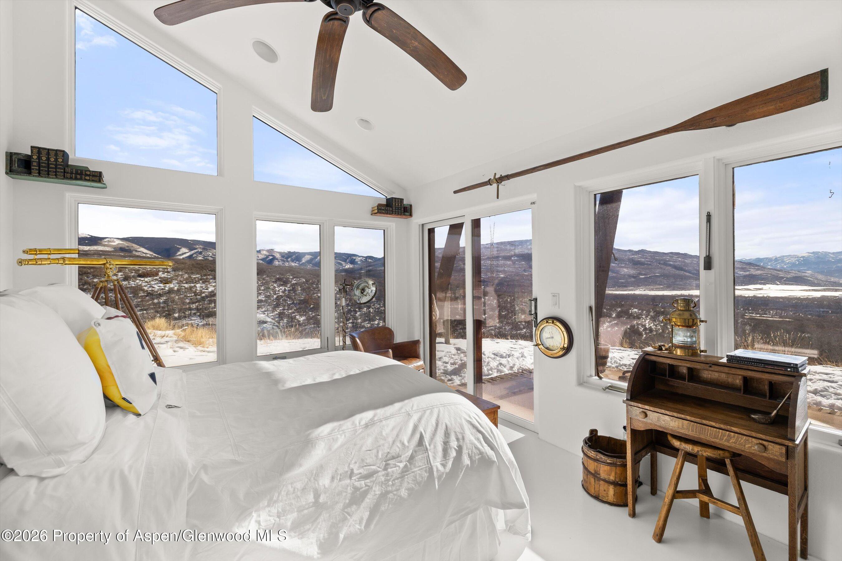 Bedroom with a white bed, brass telescope, and expansive snowy mountain views through large windows.