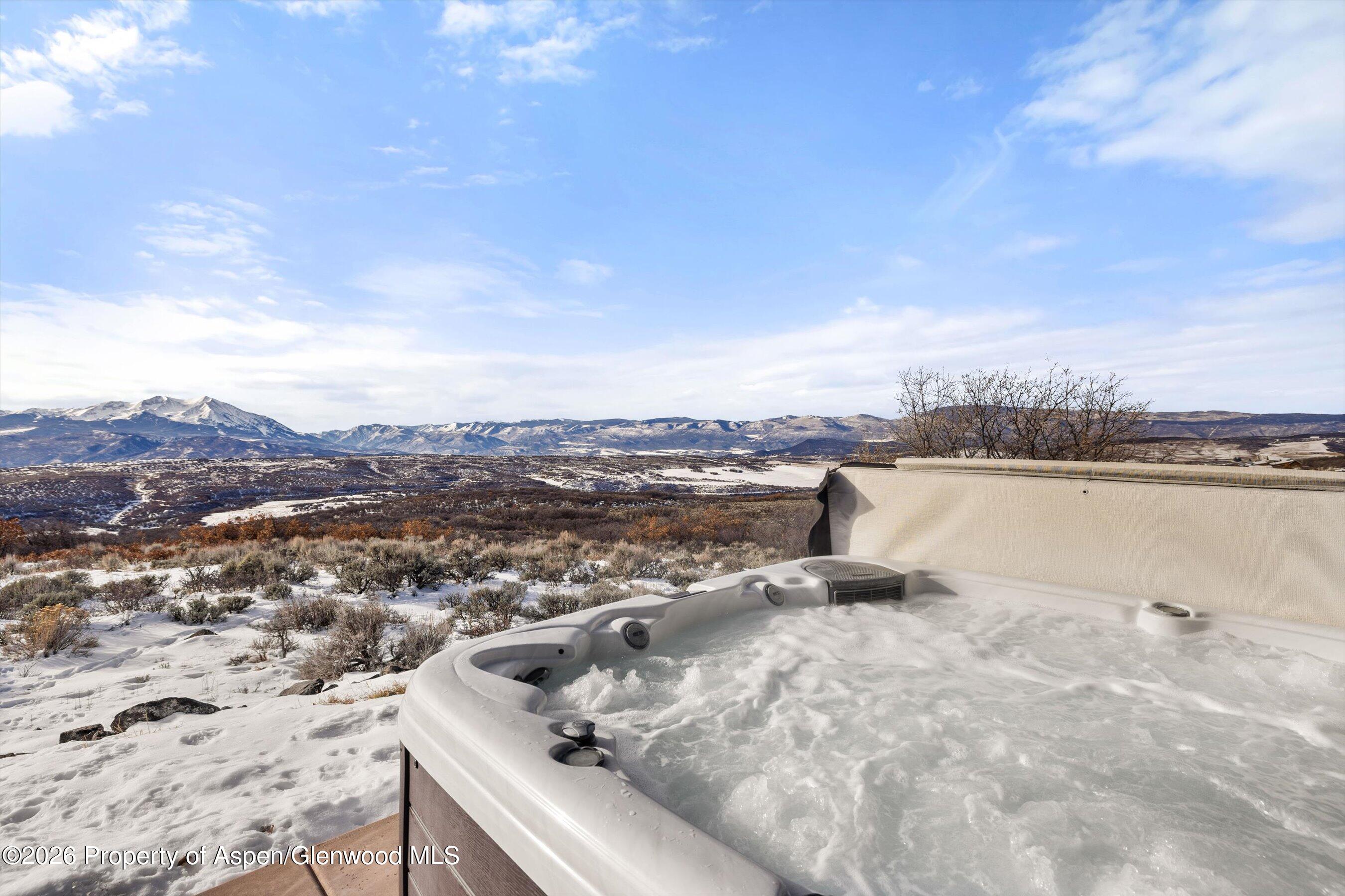 Outdoor hot tub overlooking snowy hills and a mountain range.