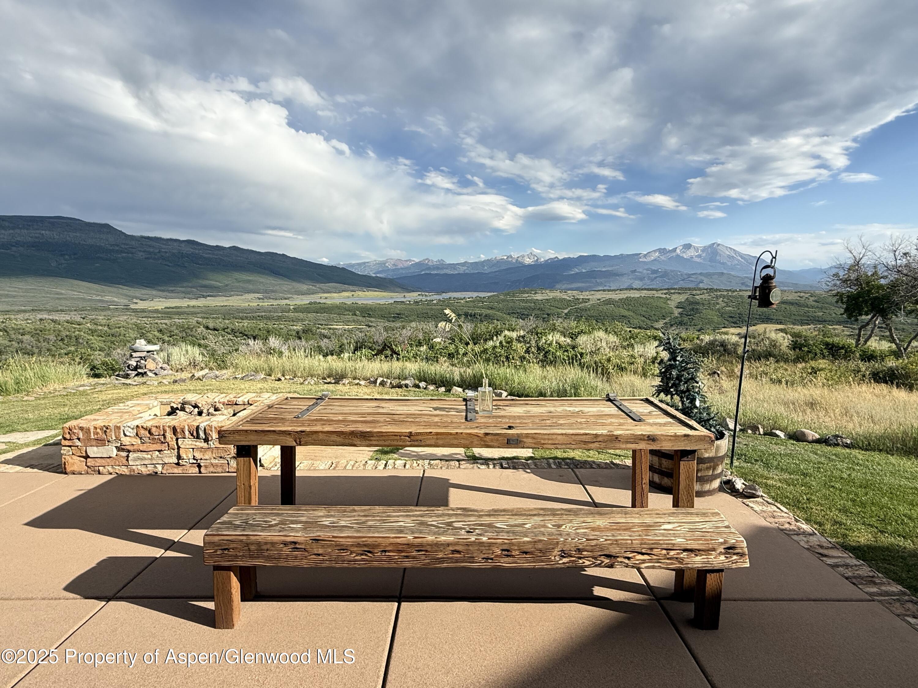 Stone patio seating overlooks a green valley and distant snow-dusted mountains.