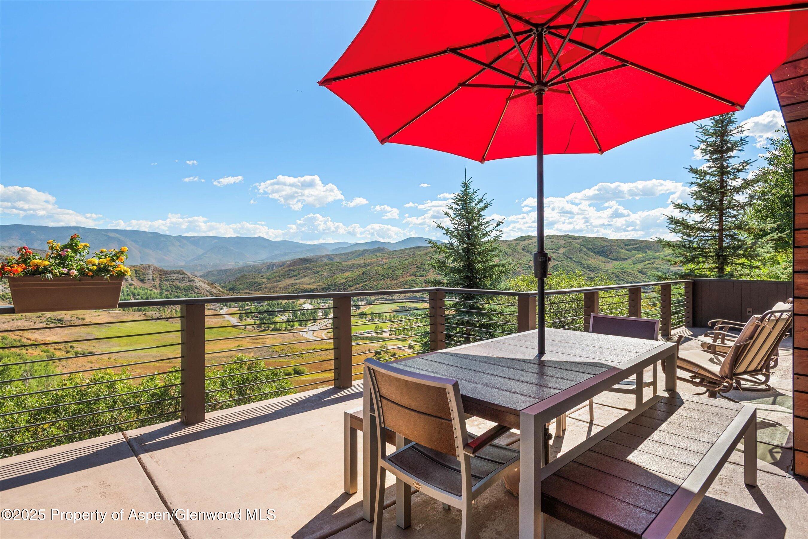 Furnished deck with a red umbrella and dining table overlooking a mountain valley.