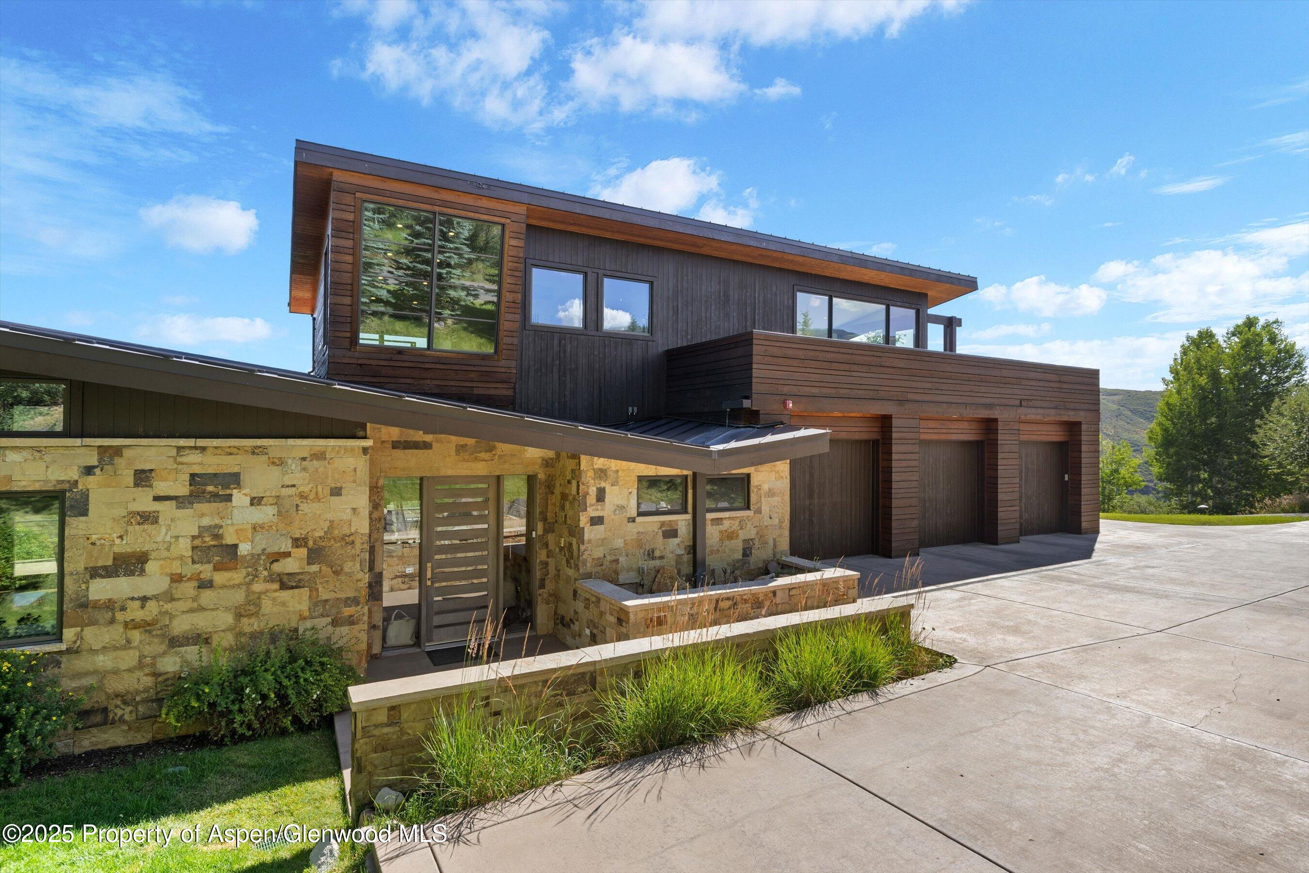 Modern wood-and-stone home with a broad driveway and three-bay garage.