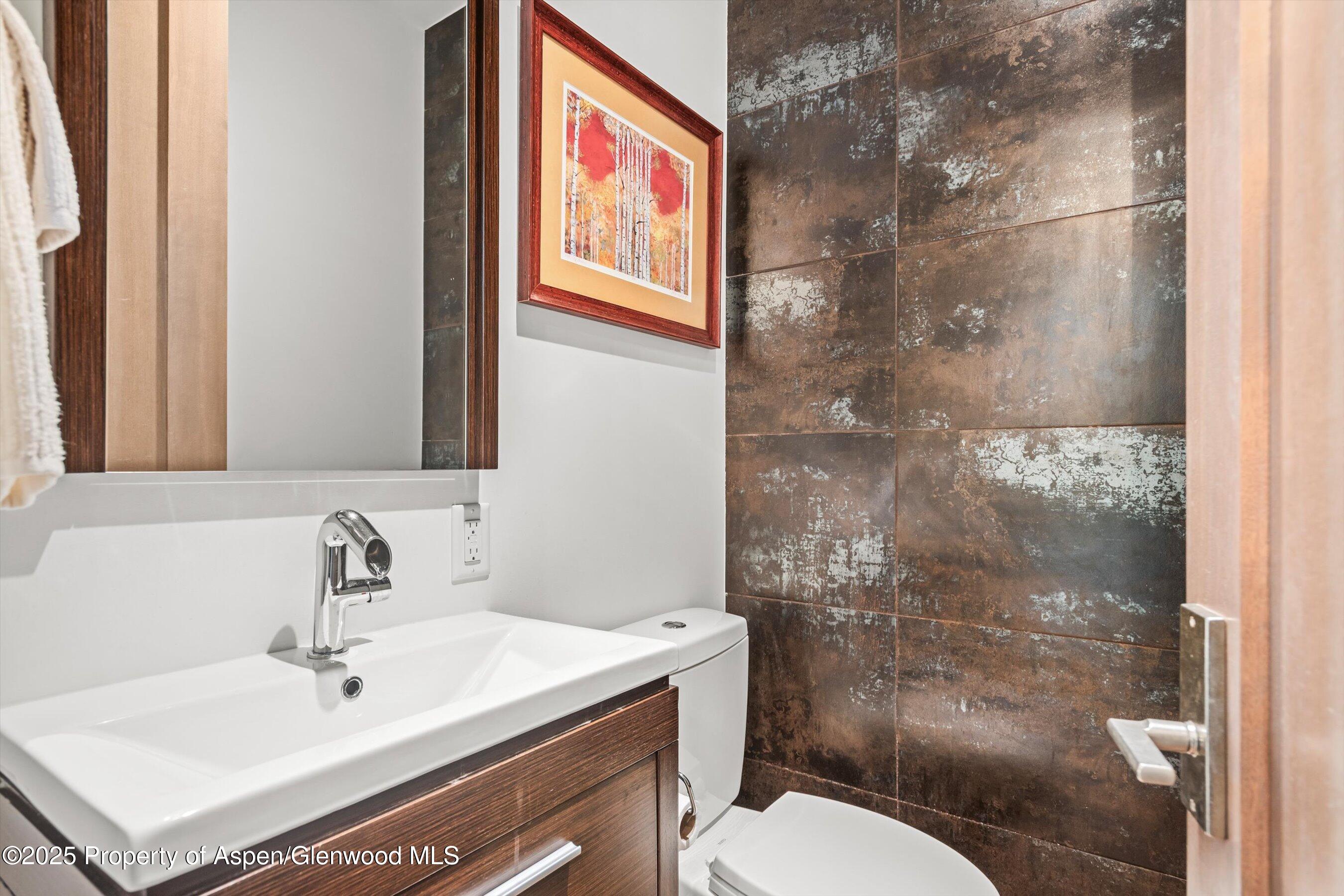 Bathroom with a white sink, dark wood vanity, and textured brown tile shower wall.