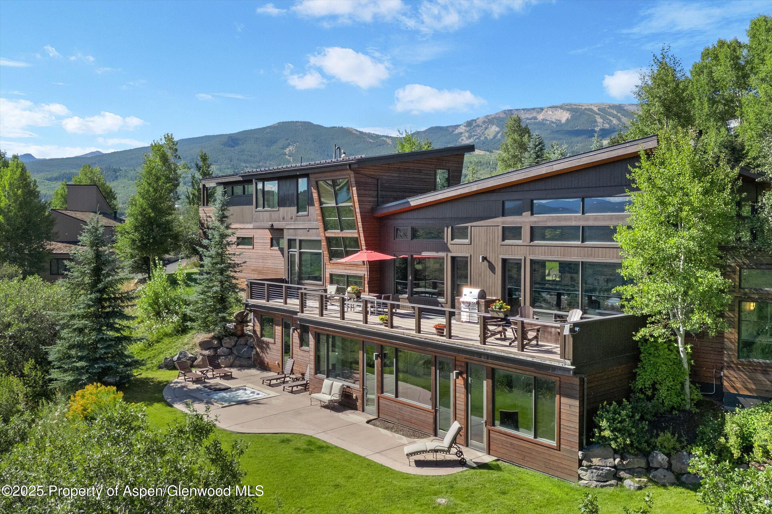 Modern mountain home with a broad deck and small pool, backed by forested mountains.