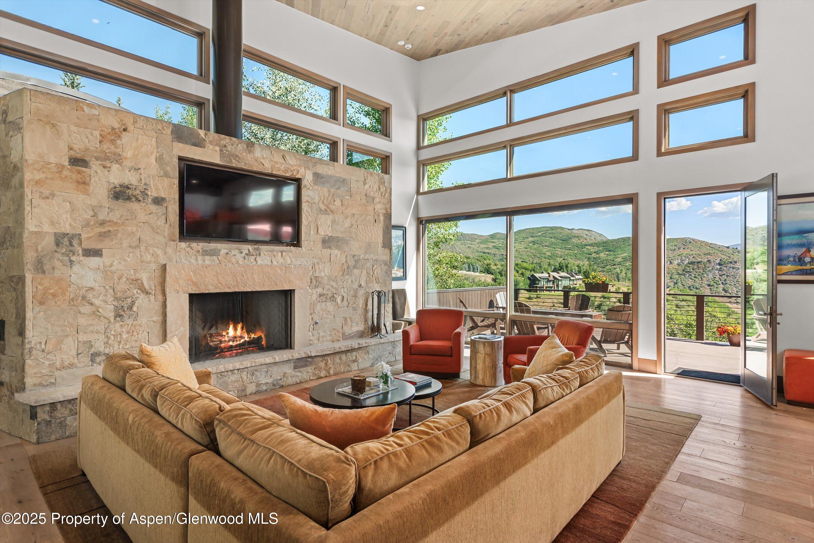 Living room with a stone fireplace, tall windows, and mountain views from the adjoining deck.