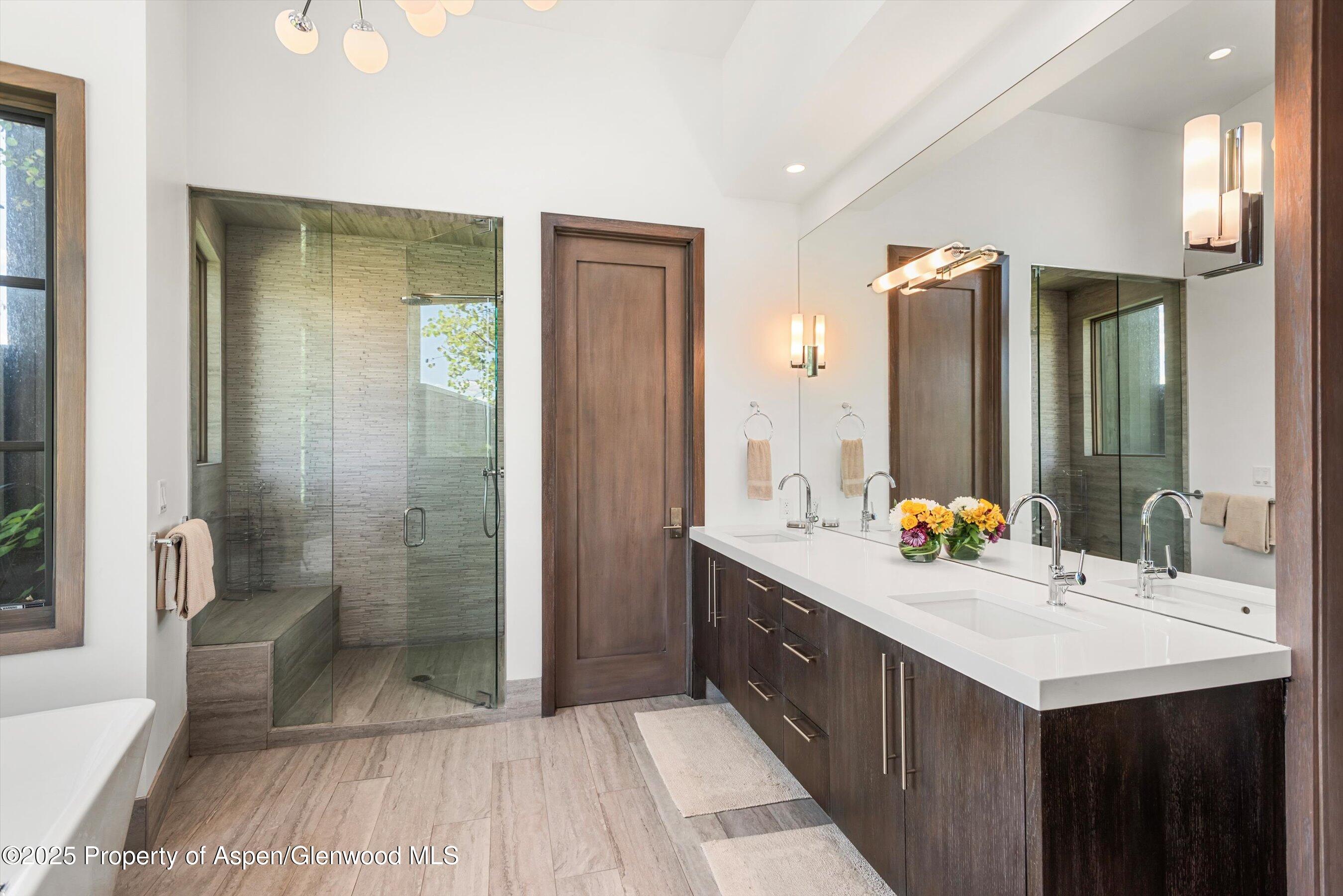 Contemporary bathroom with a glass shower, dark wood double vanity, large mirror, and freestanding tub.