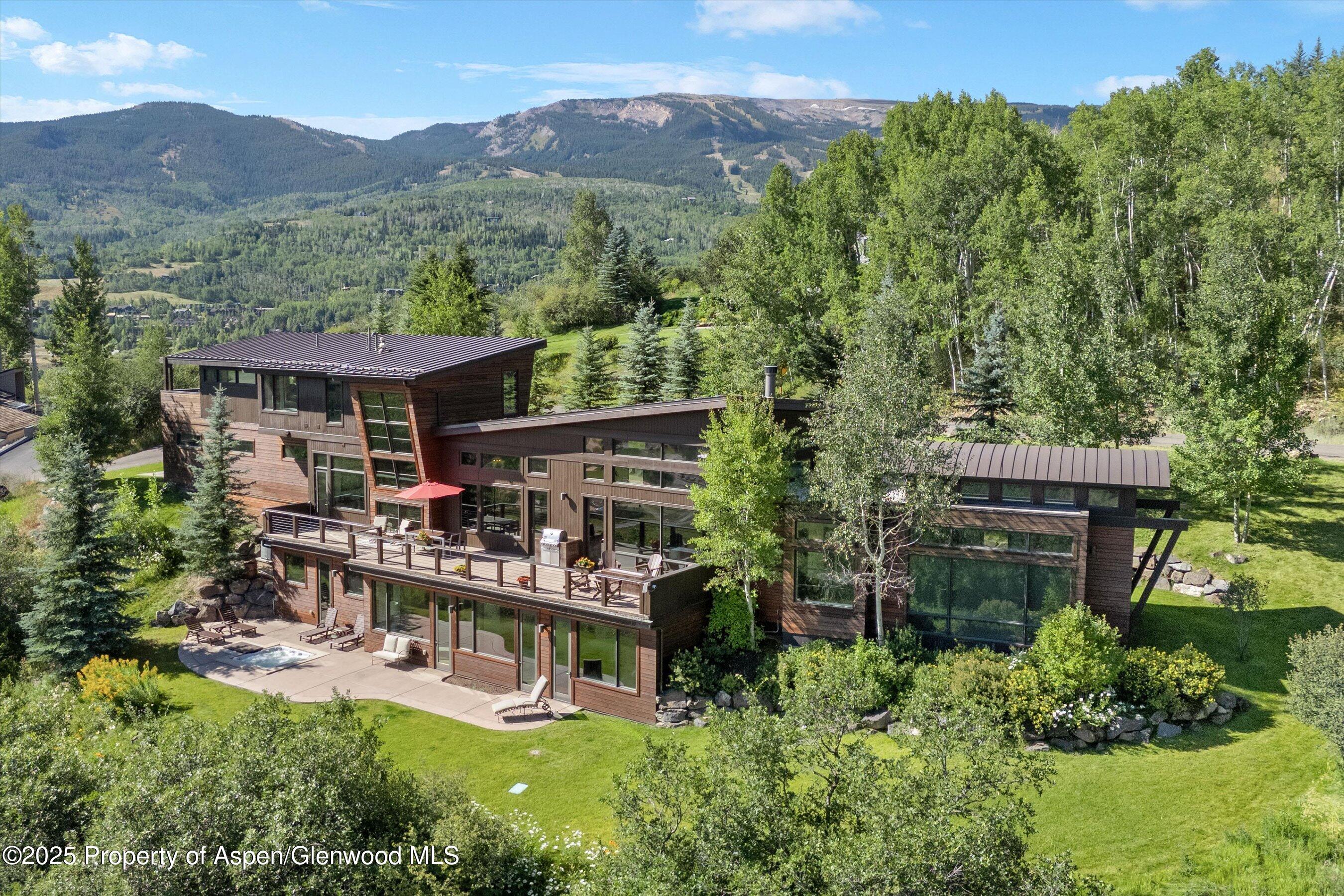 Modern wood-and-glass home with expansive decks, lawn, and mountain views.