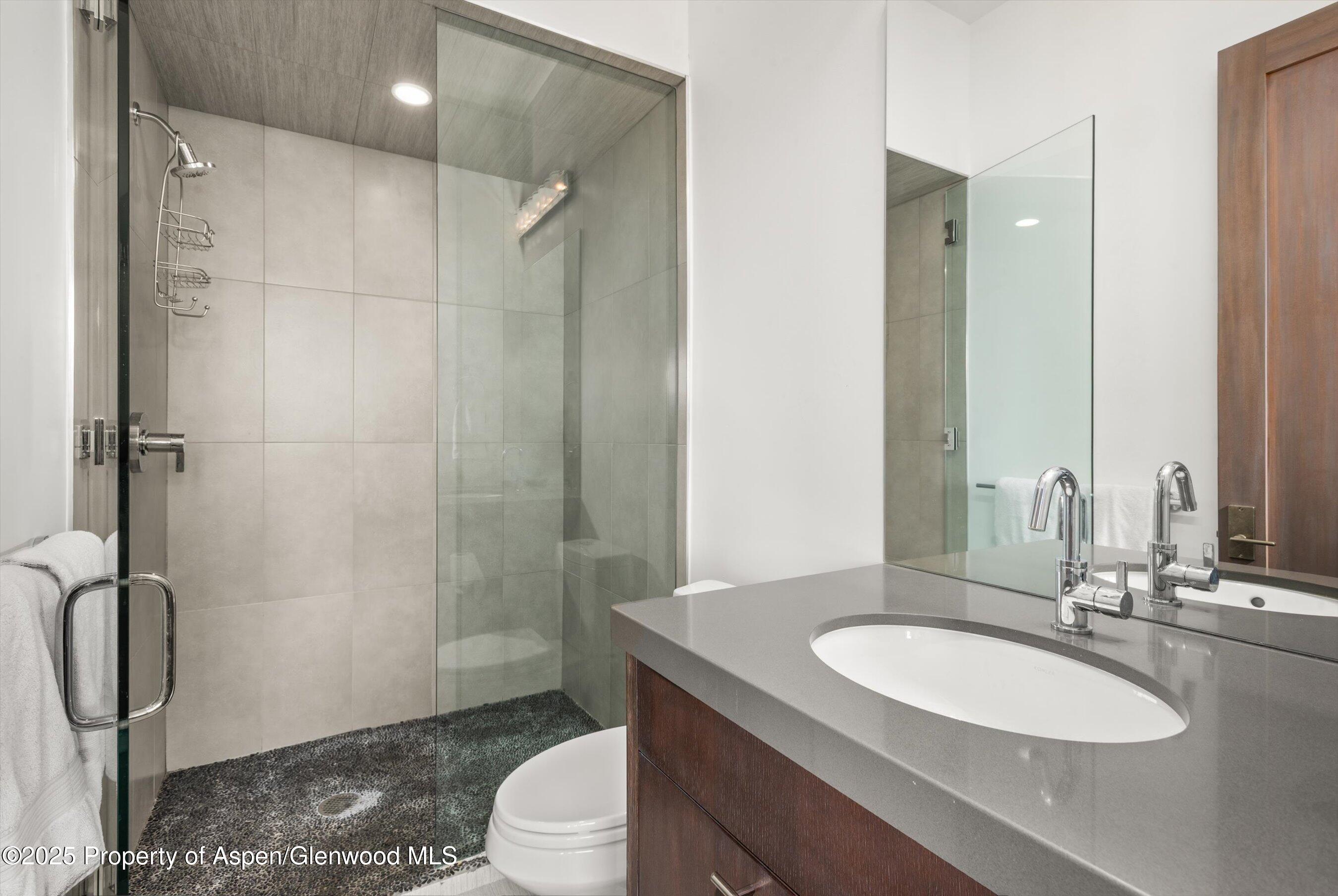 Modern bathroom with a glass walk-in shower, dark pebble floor, and wood vanity.