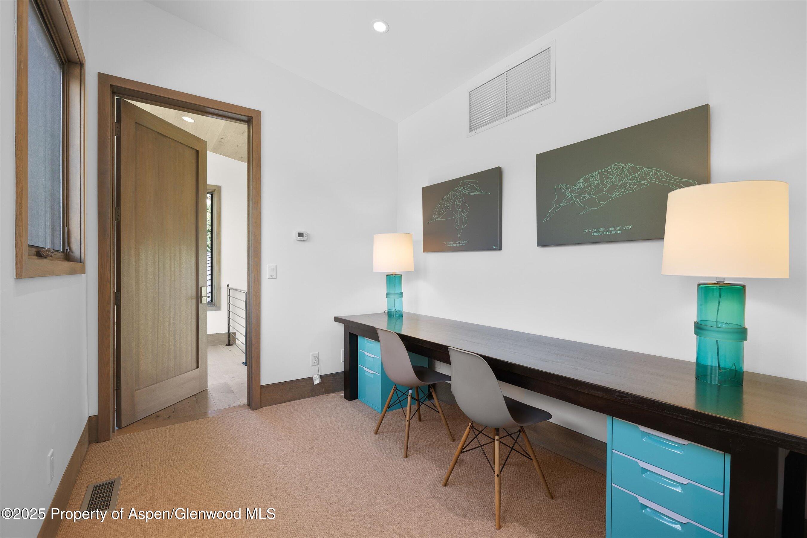 Home office with a long desk, turquoise drawers, two chairs, and mountain artwork.