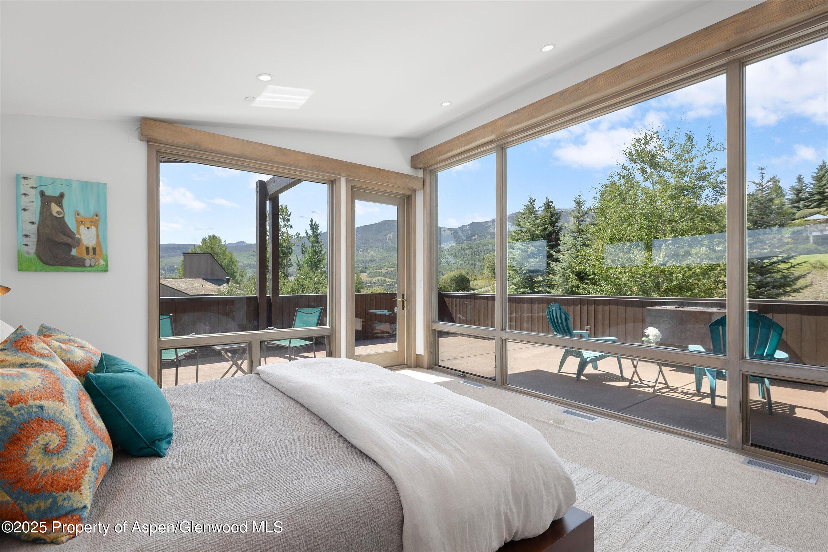 Bedroom with floor-to-ceiling windows overlooking a deck and mountain views.