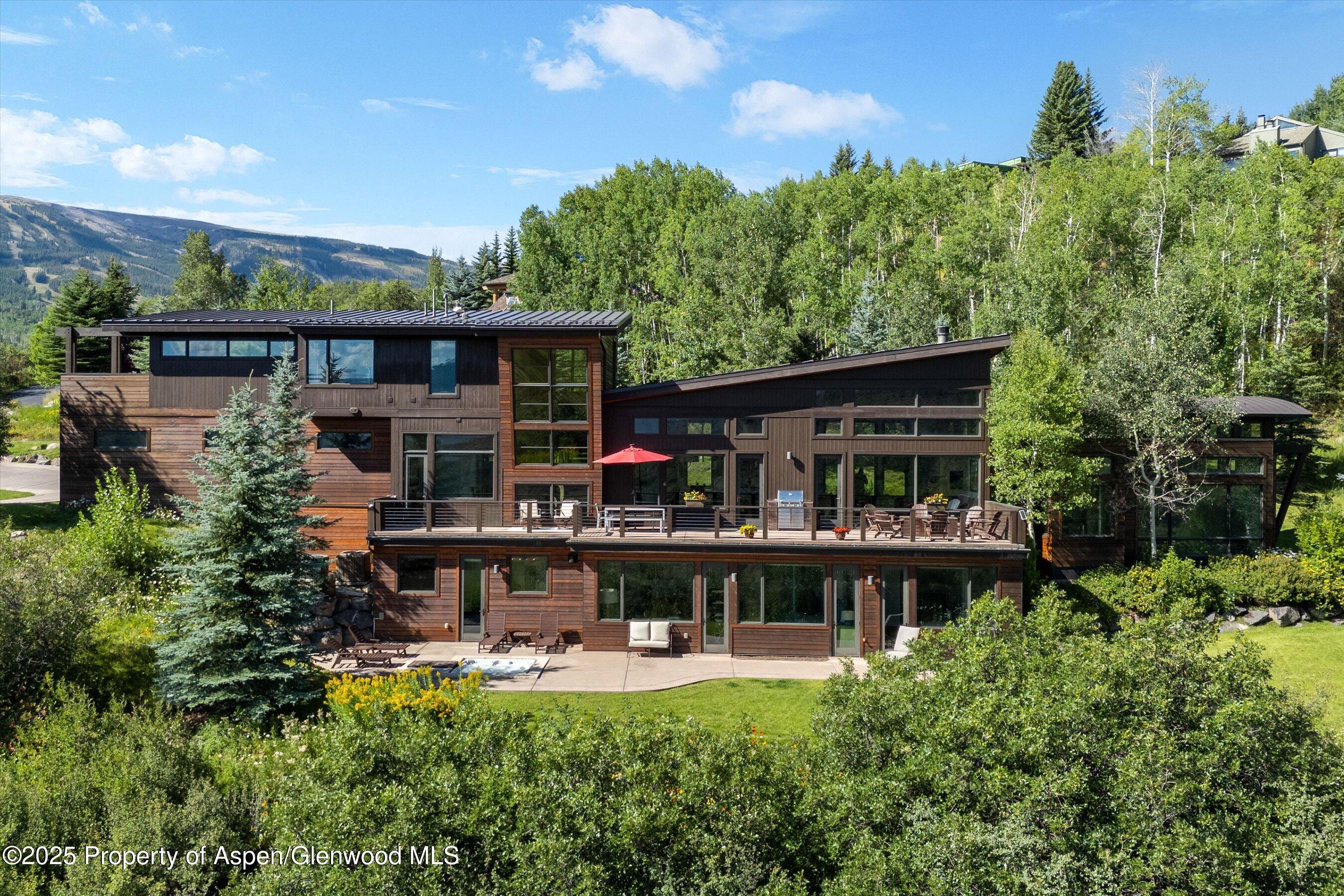 Modern wood-sided home with a broad deck, surrounded by trees and mountain scenery.