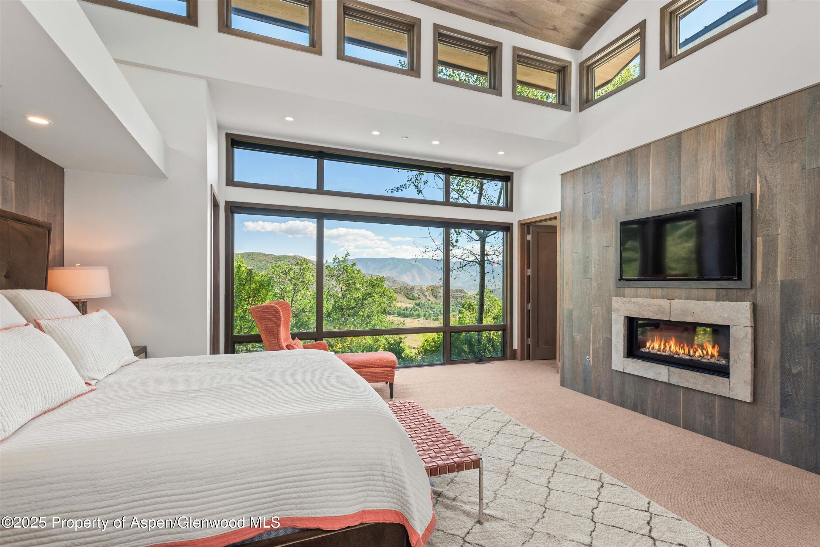 Bedroom with vaulted ceiling, mountain views through large windows, and a fireplace.