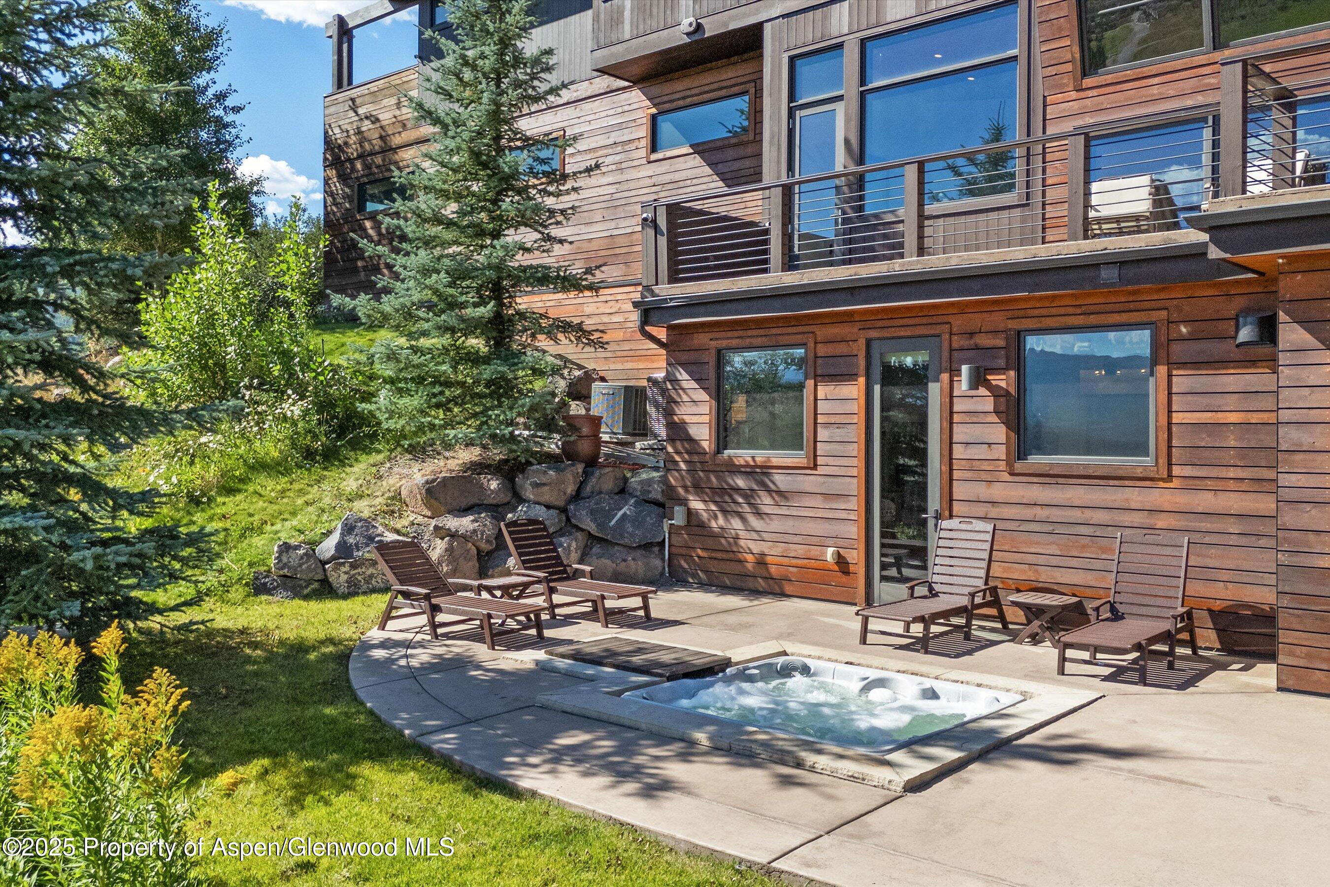 Wood-sided home with a patio, lounge chairs, and an in-ground hot tub among trees.