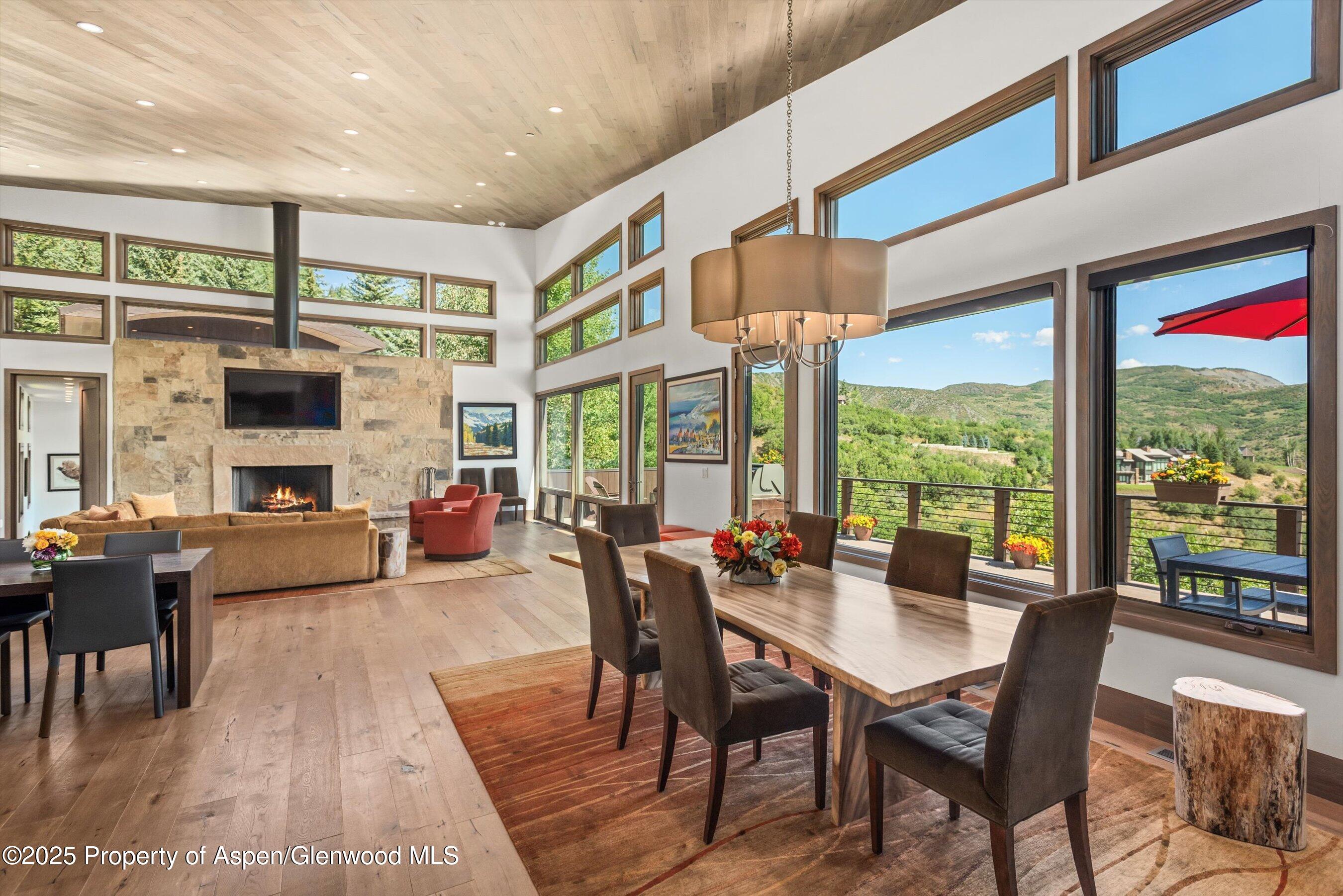 Open living and dining room with a stone fireplace, tall windows, and mountain views.