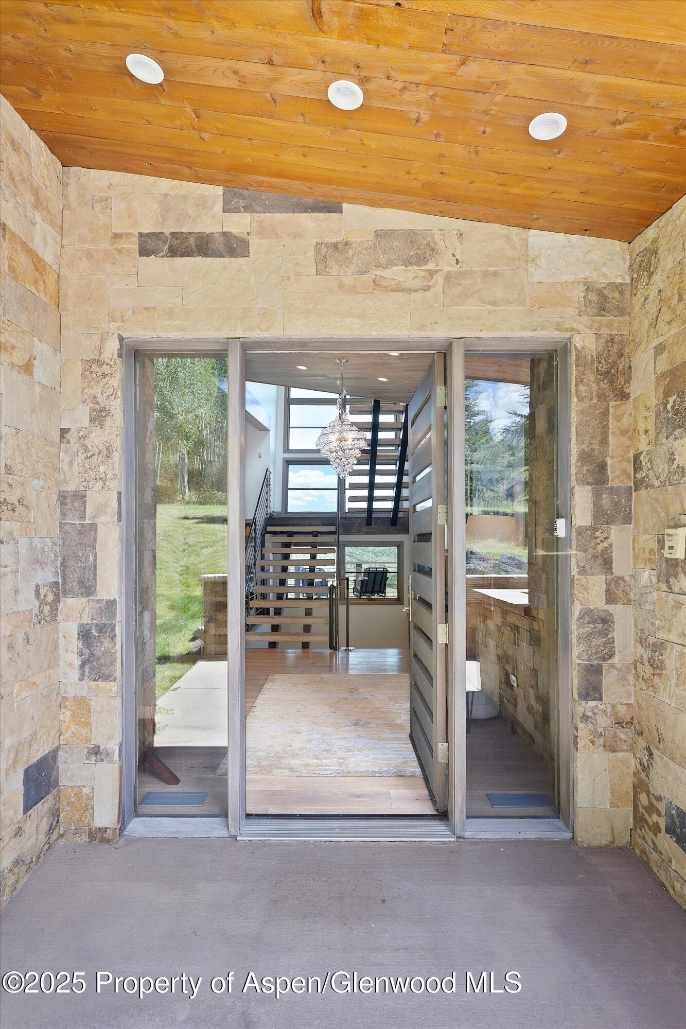 Stone-clad home entrance opens to a bright foyer with an open staircase and chandelier.