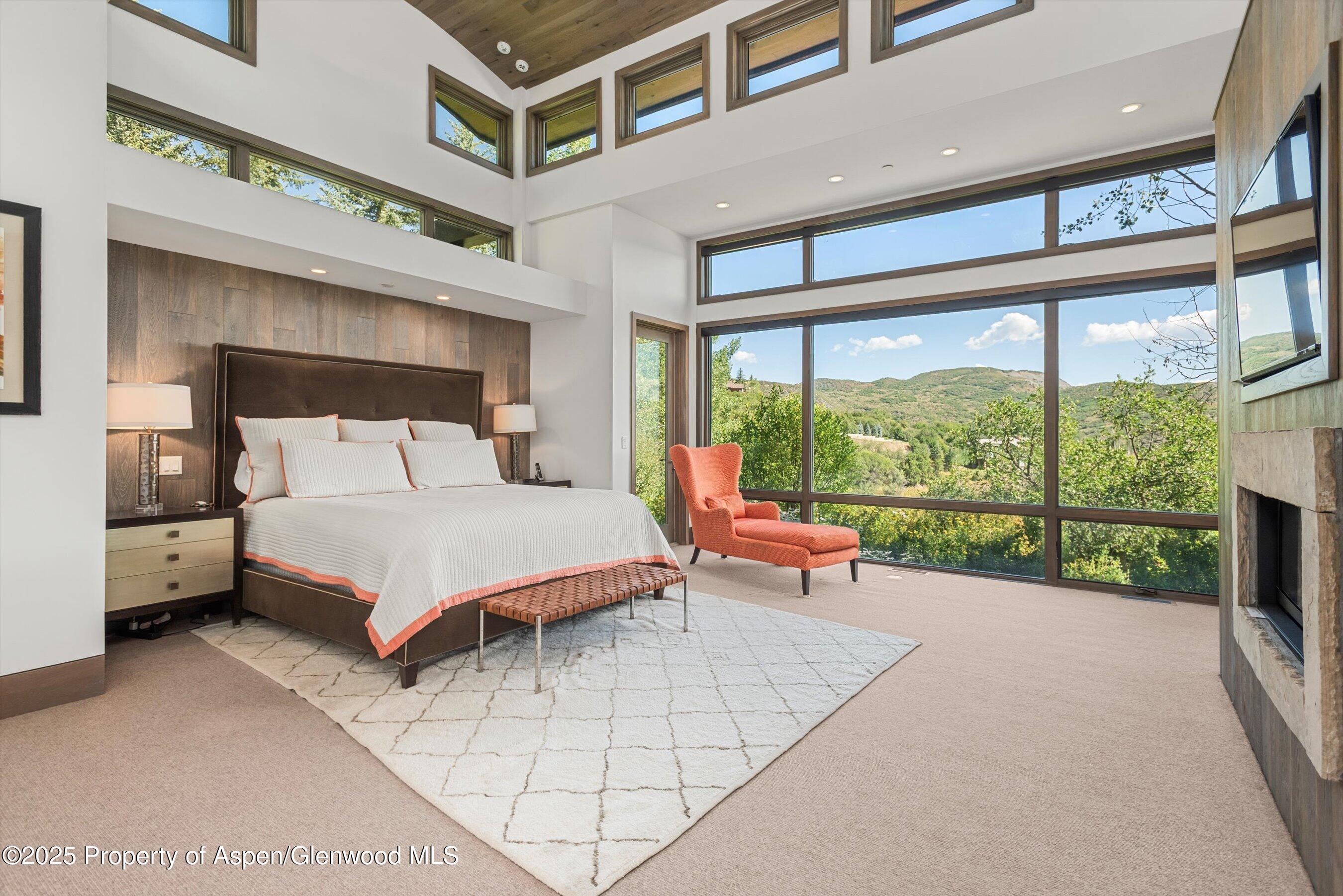 Bedroom with vaulted wood ceiling, floor-to-ceiling windows, and views of green hills.