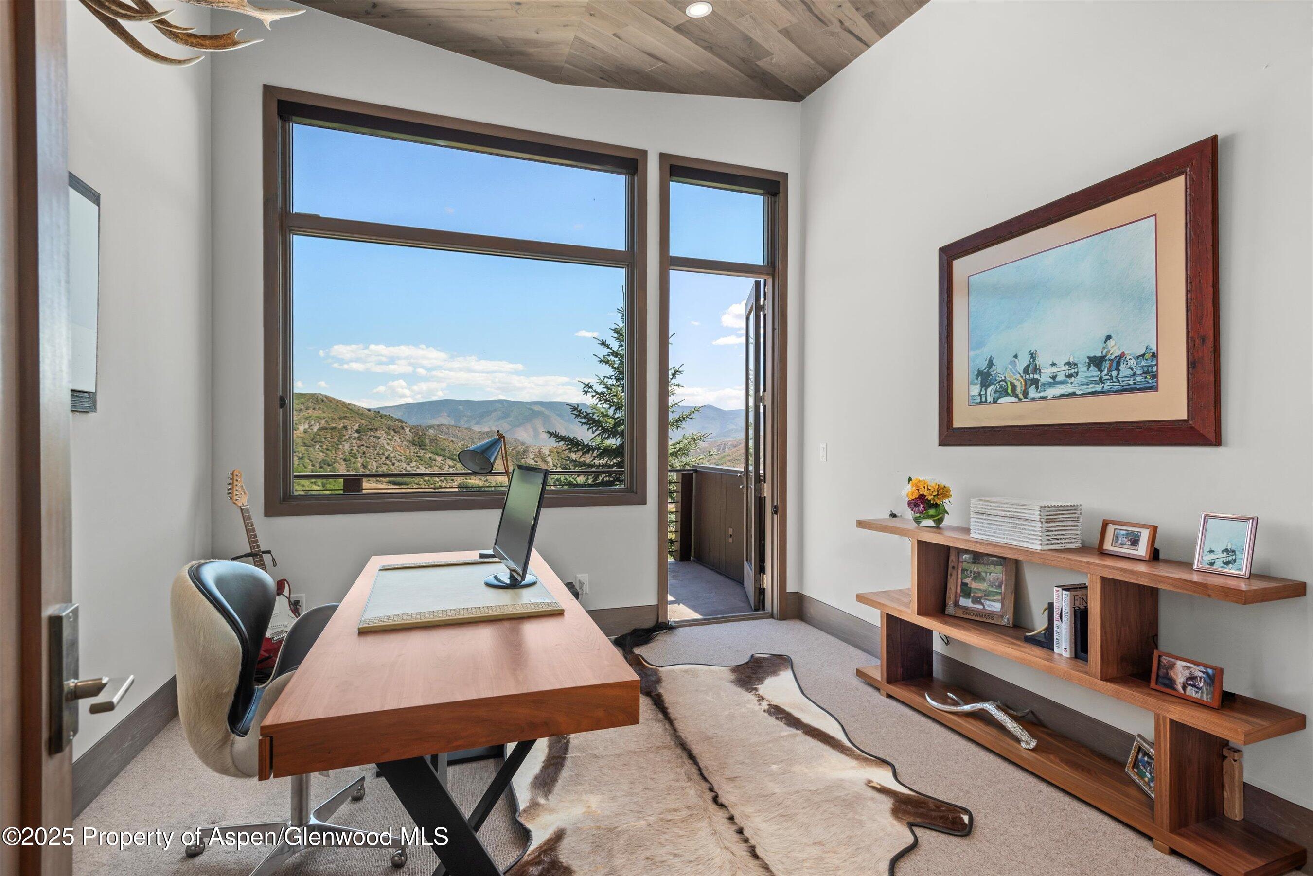 Furnished home office with a wooden desk and mountain views through large windows.