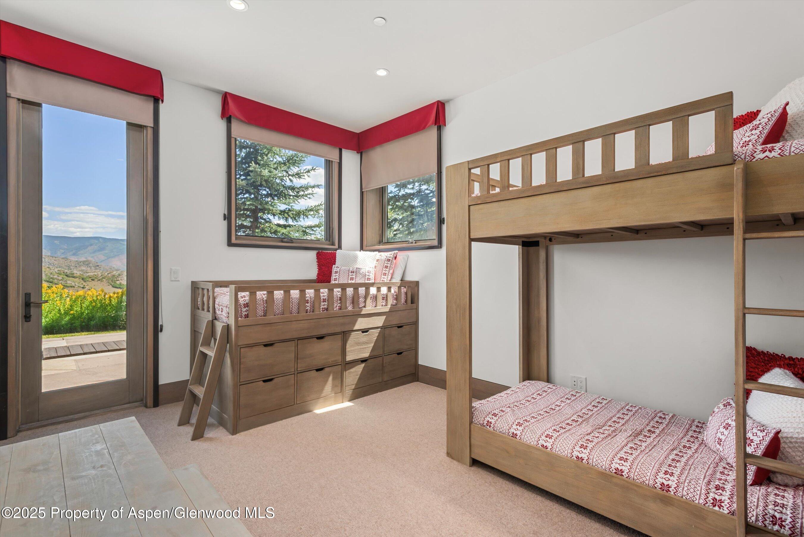Bedroom with wooden bunk beds and a storage daybed, overlooking mountains through the windows.