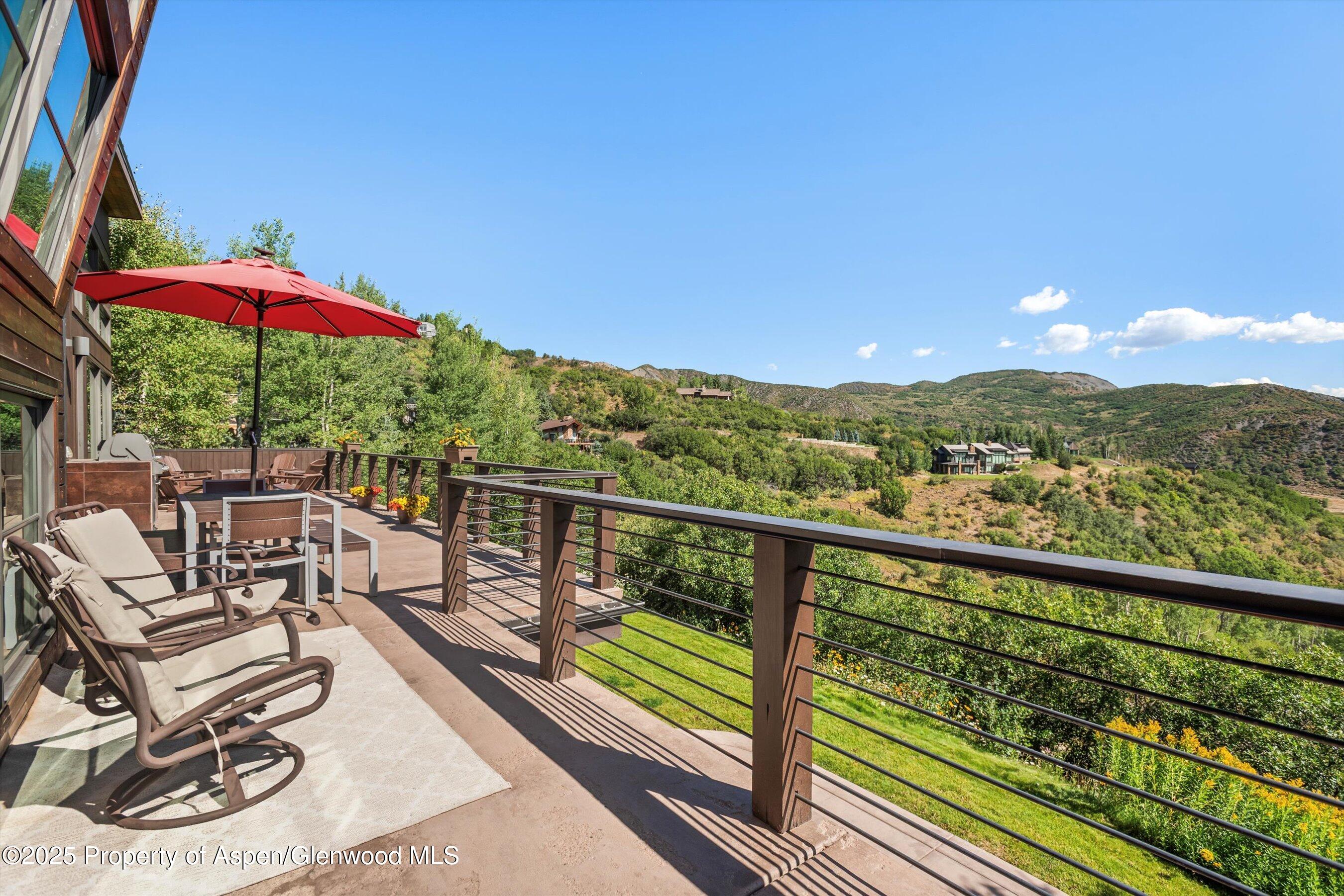 Furnished deck with a red umbrella overlooking green hills and mountain ridges.
