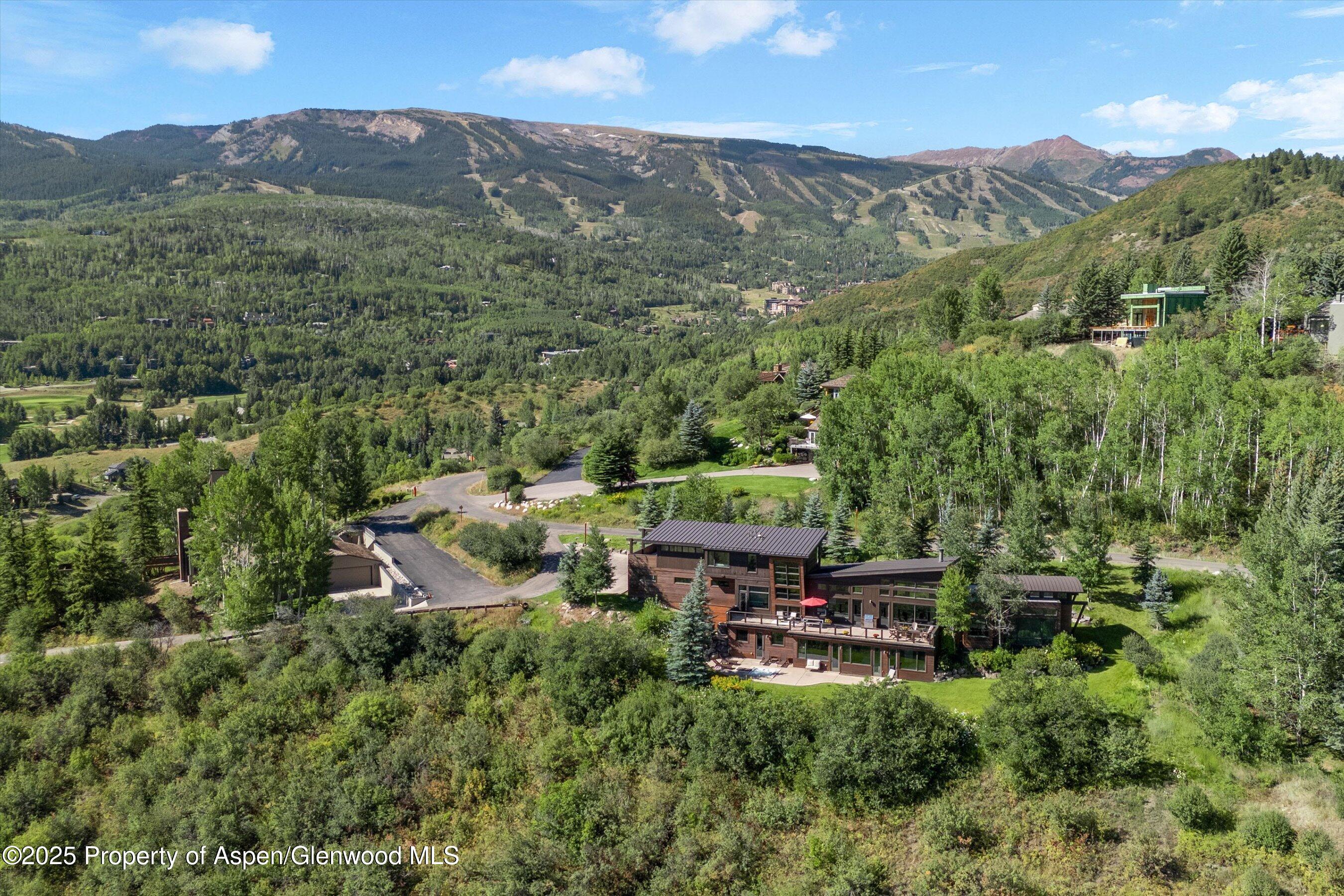 Modern mountain home among trees, overlooking a broad valley with ski trails.