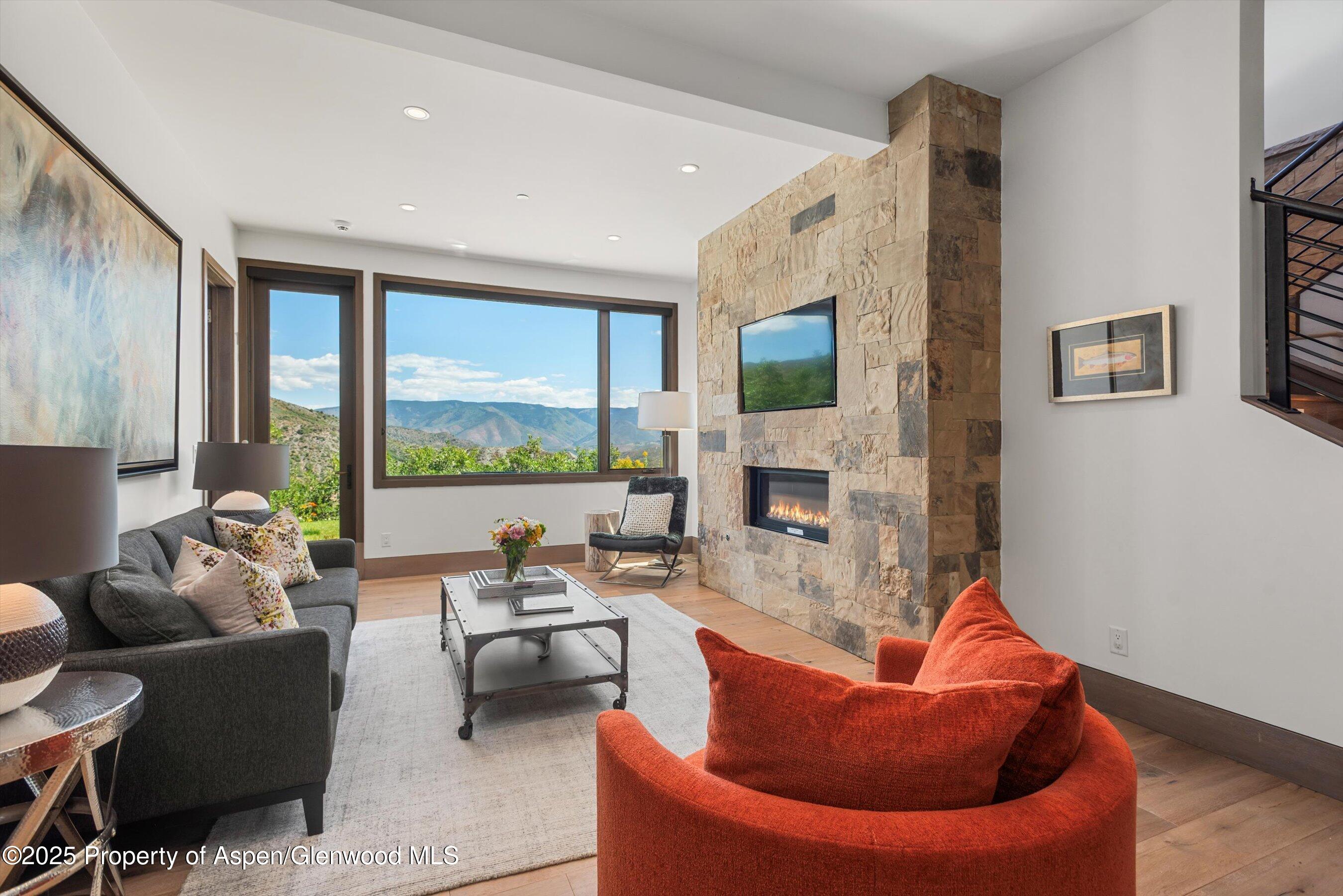 Living room with a stone fireplace, rust-colored chair, and mountain views through large windows.