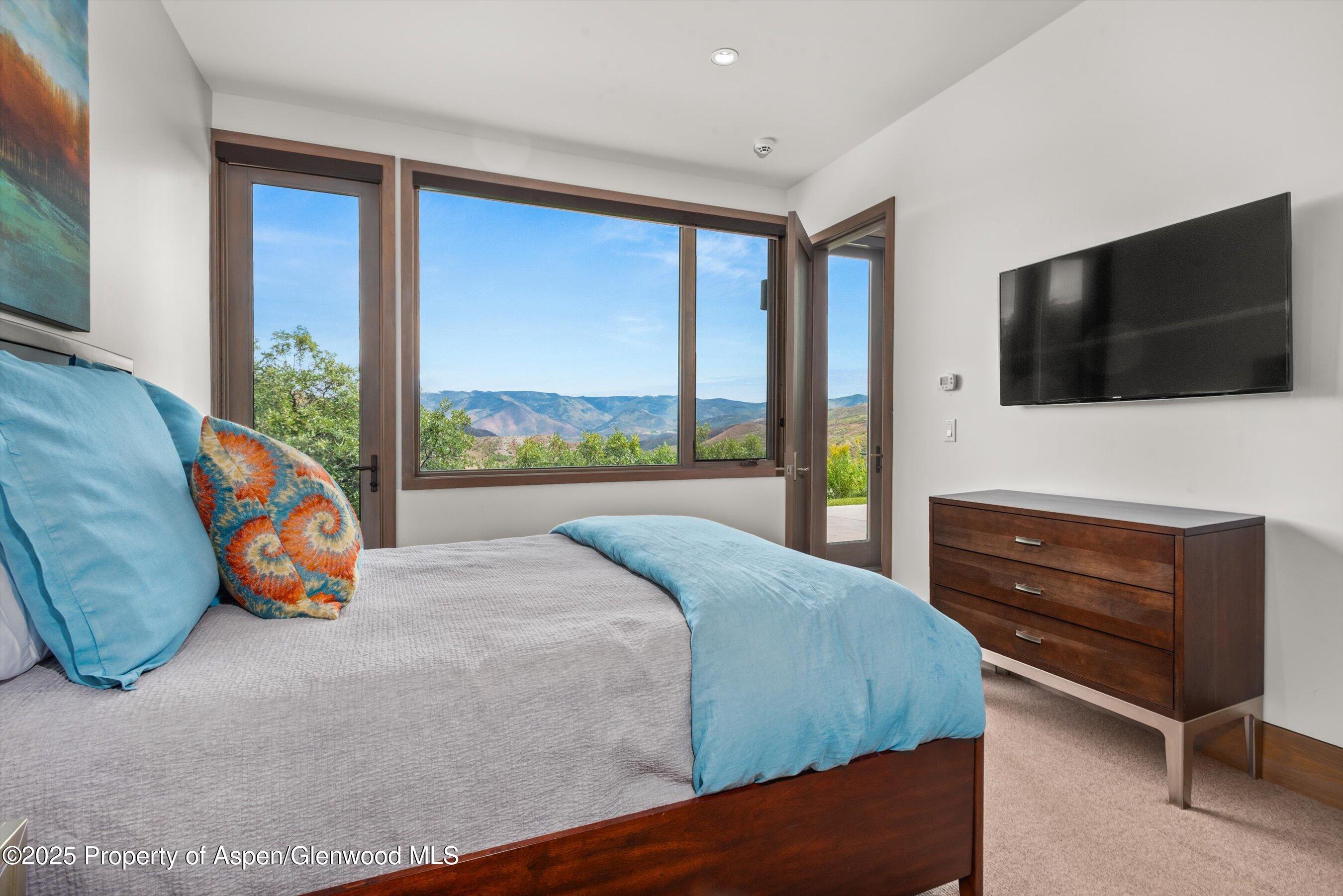 Furnished bedroom with blue accents and large windows overlooking mountain ridges.