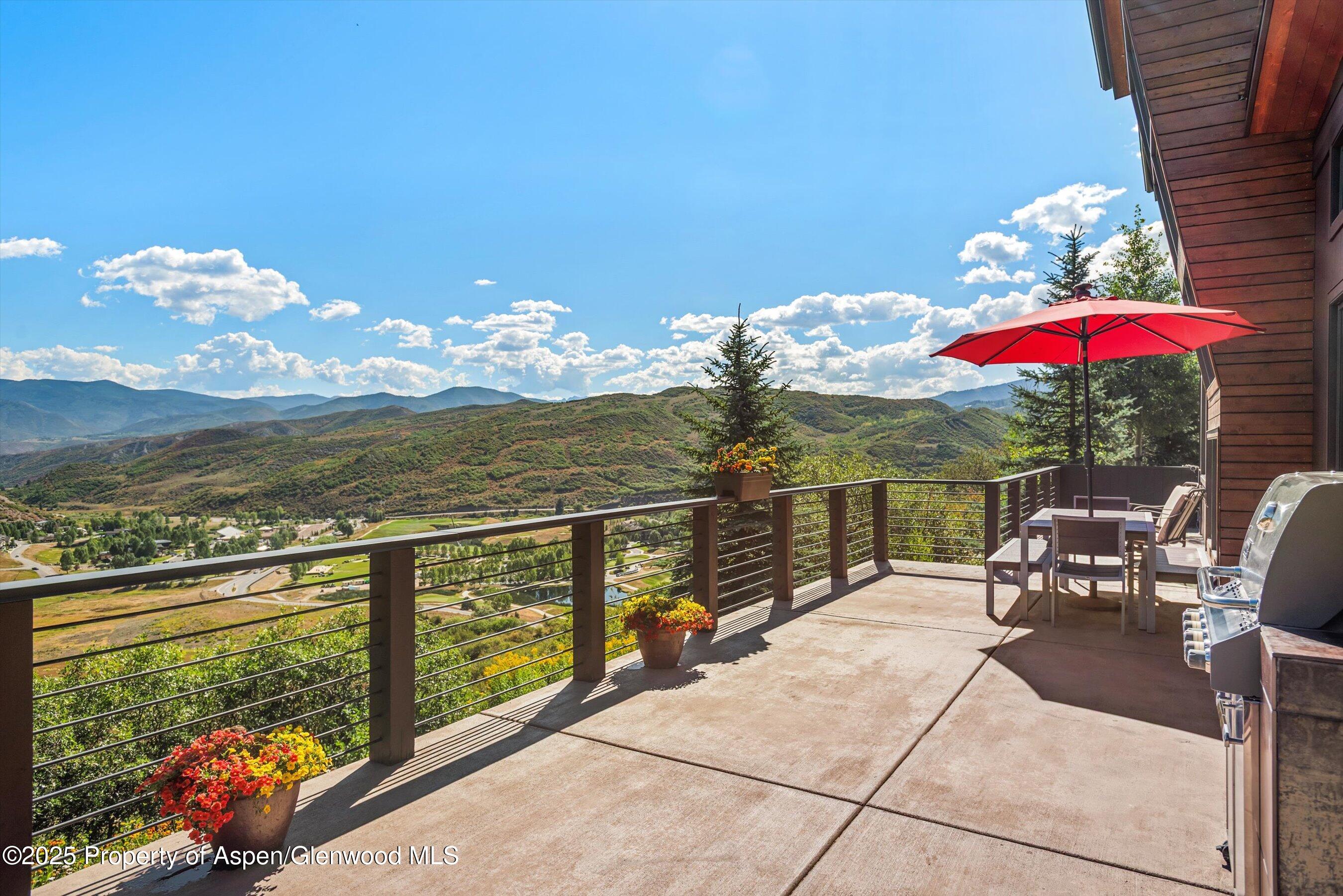 Mountain-view deck with dining set, red umbrella, flower planters, and stainless steel grill.