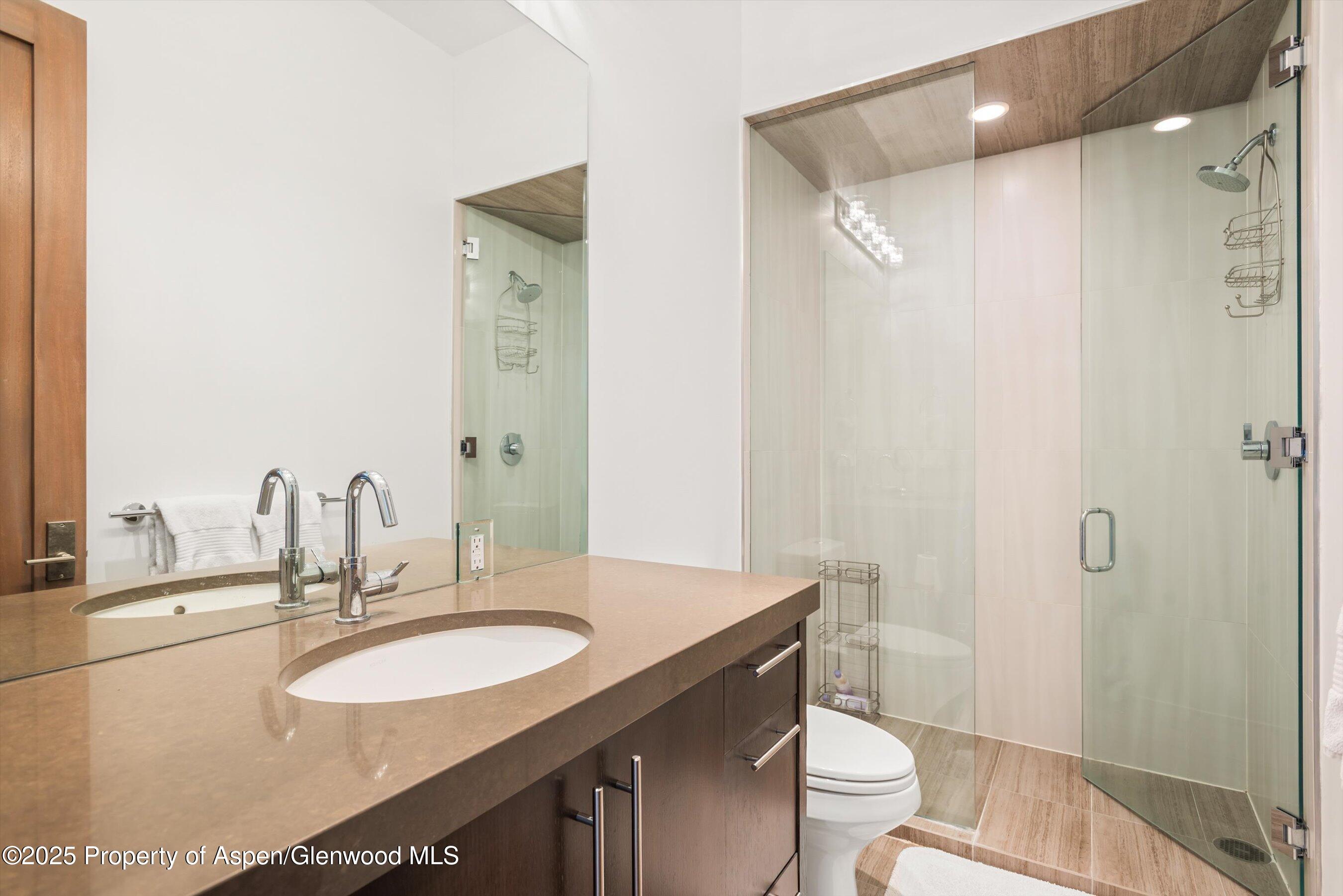 Modern bathroom with a long stone vanity and glass shower beneath a wood-look ceiling.