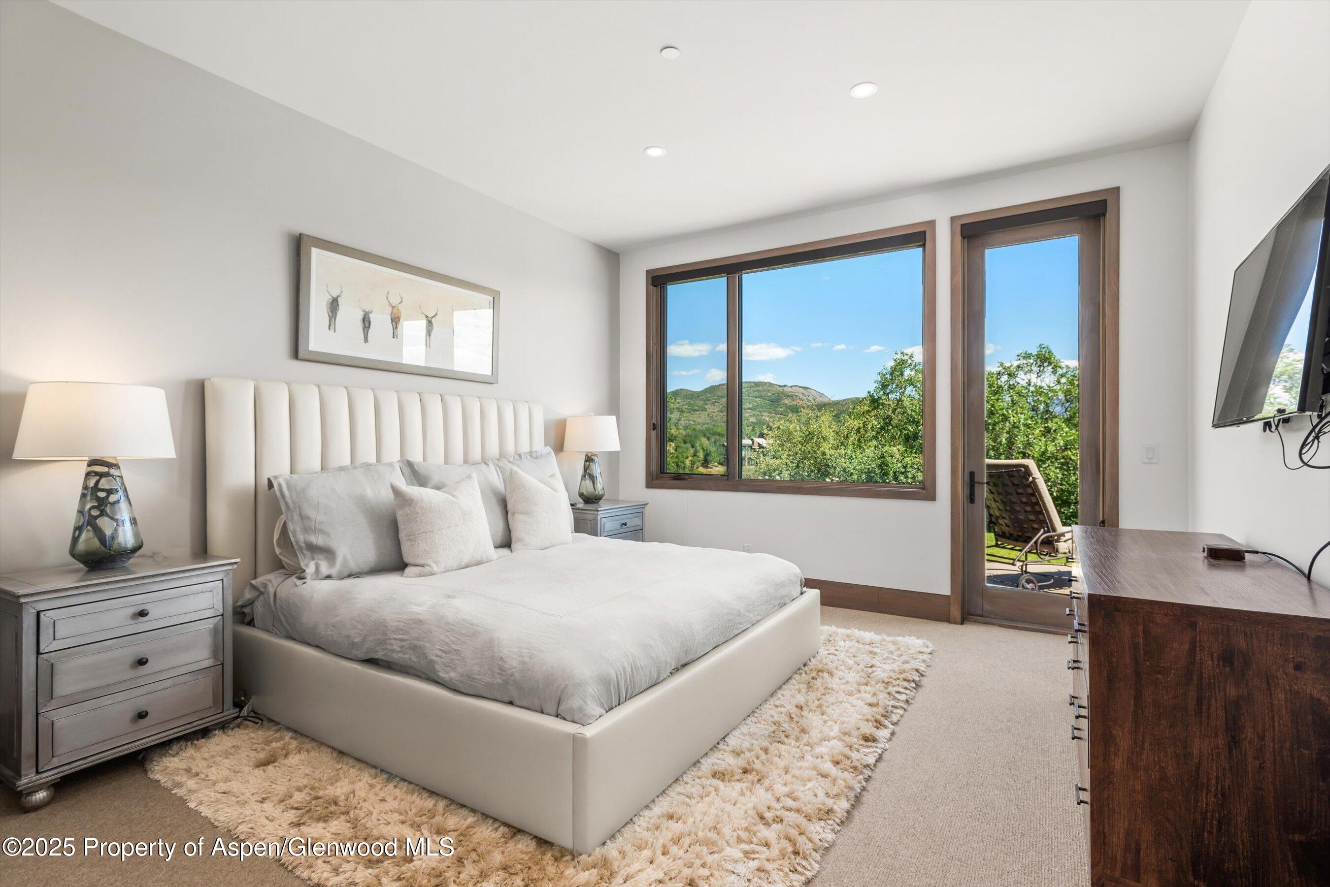 Bedroom with a white upholstered bed and windows overlooking green mountains.