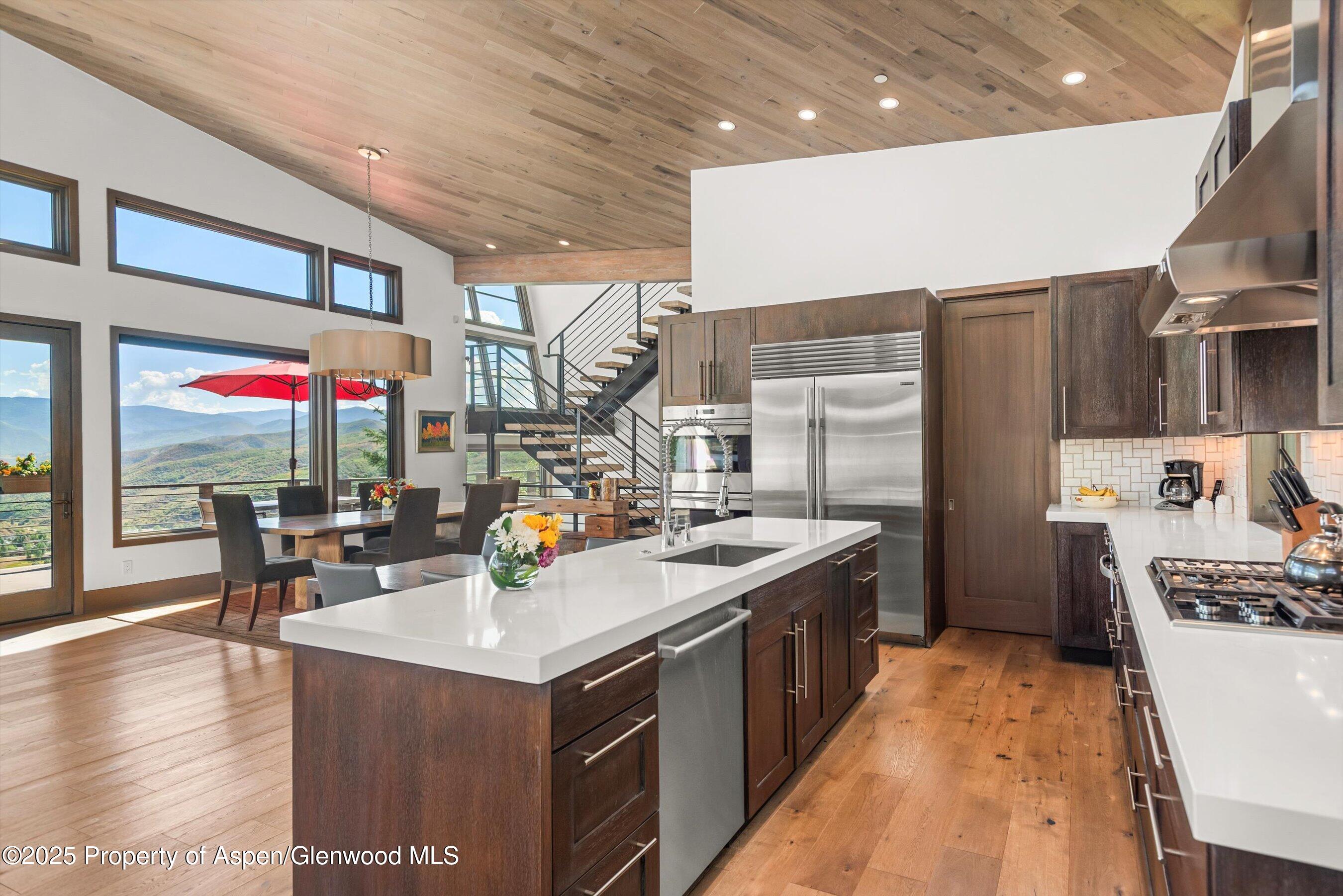 Modern kitchen with a large island, stainless appliances, and mountain views through expansive windows.