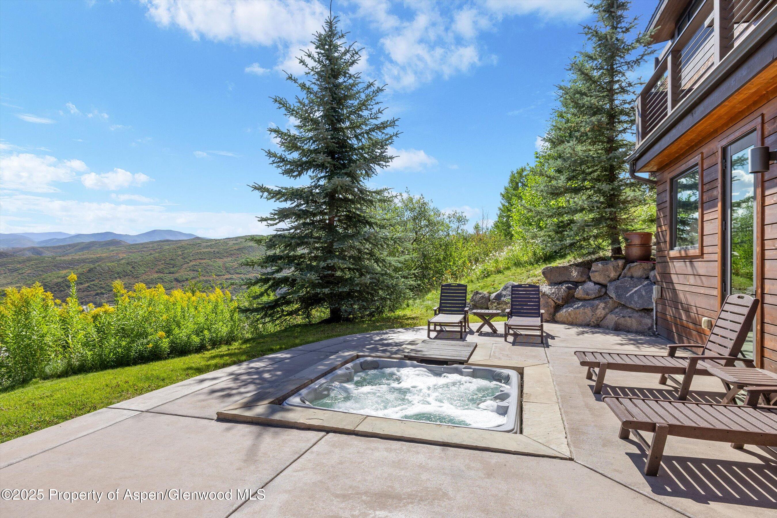 Mountain home patio with a bubbling hot tub, lounge chairs, and broad hillside views.