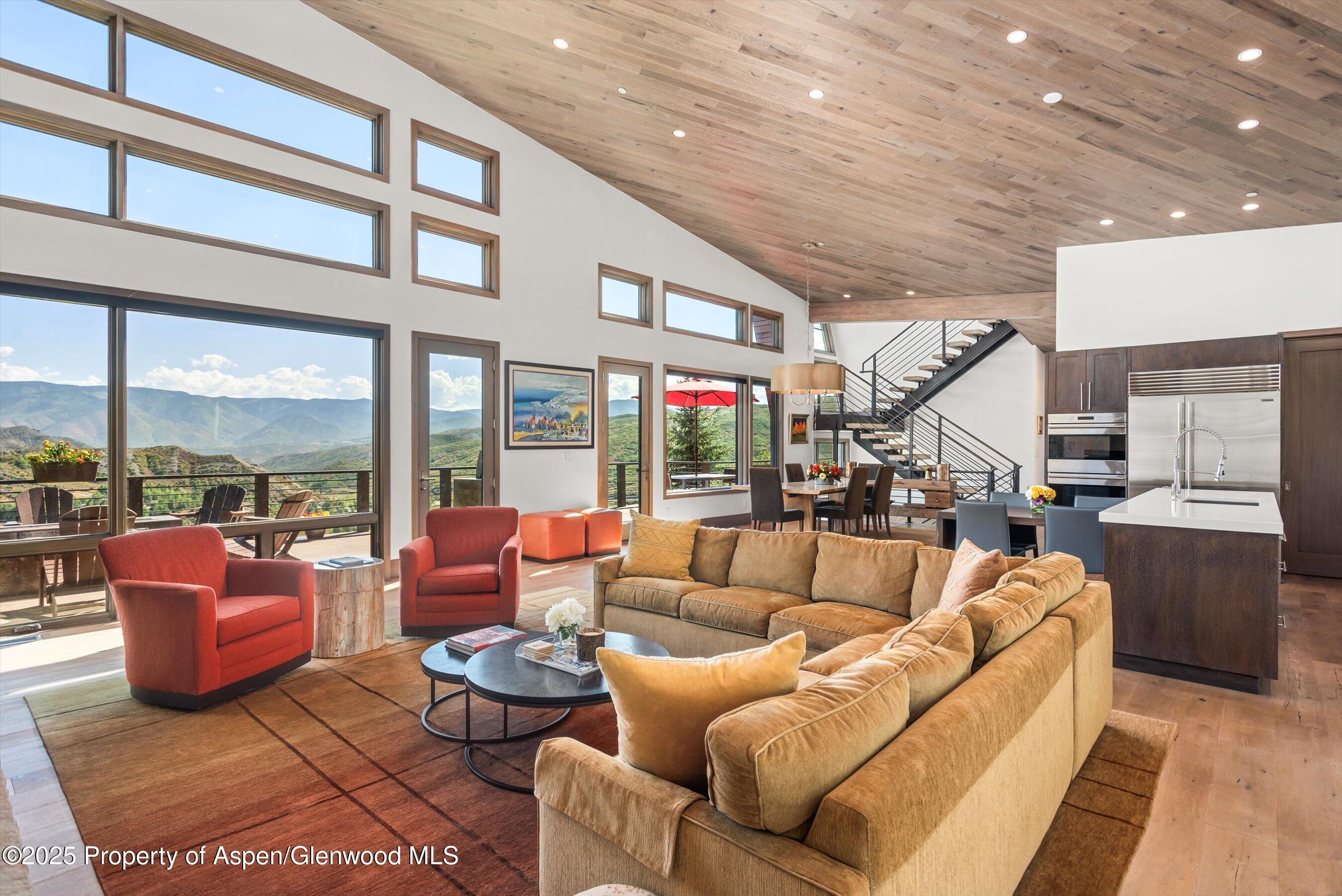 Open-plan living room with vaulted wood ceiling, mountain-view windows, and a modern kitchen.